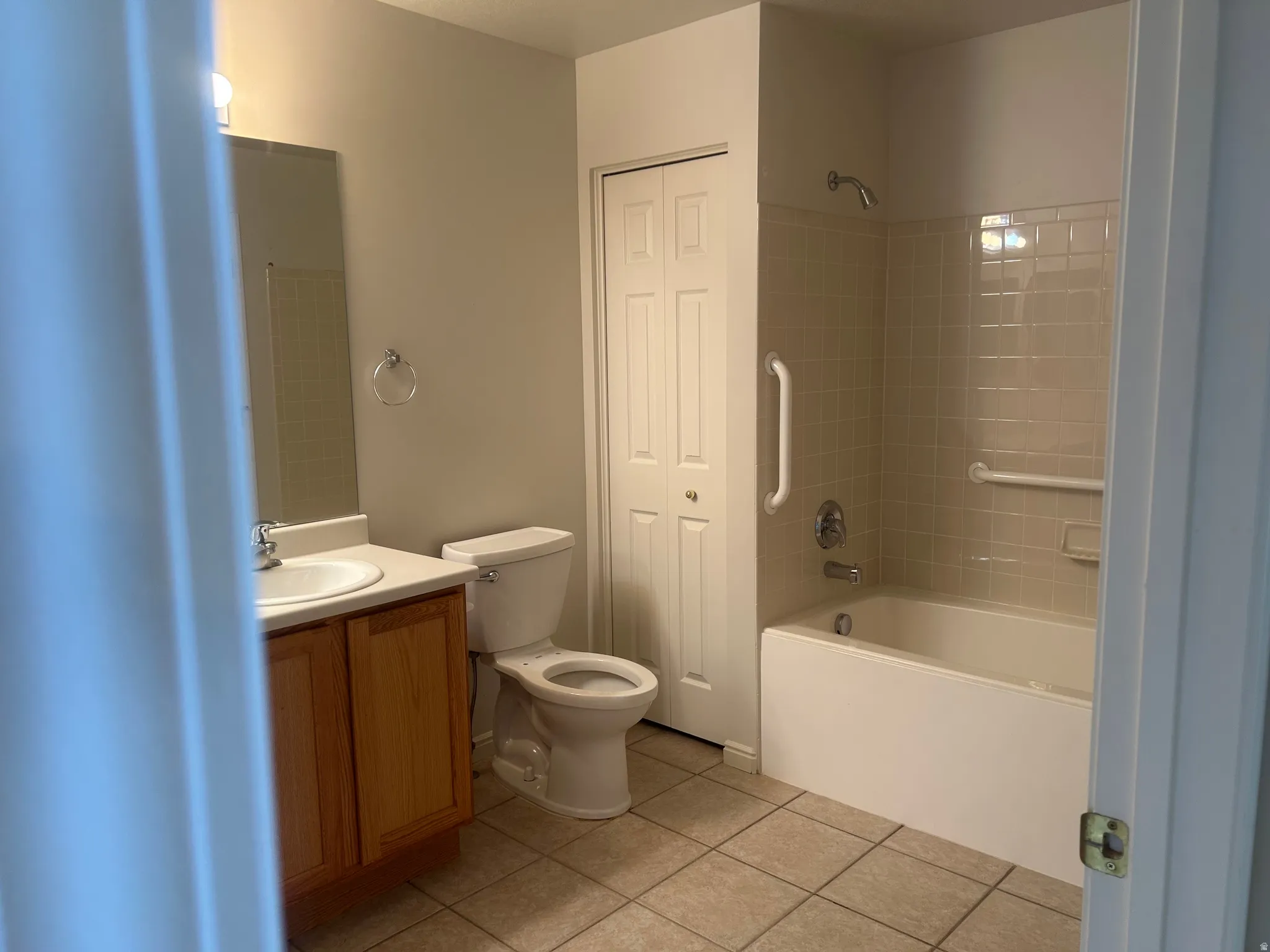 Neutral-toned bathroom featuring a tub/shower combination with subway tile surround and grab bars, a wood-finish vanity with an integrated sink, a toilet, and tiled flooring