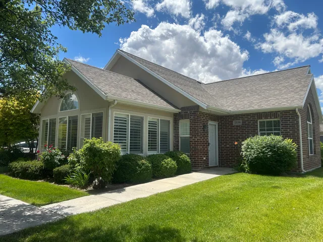 Exterior showcasing brick and stucco facade, a prominent sunroom with plantation shutters, a gabled roofline, a concrete walkway, and a manicured lawn with mature landscaping