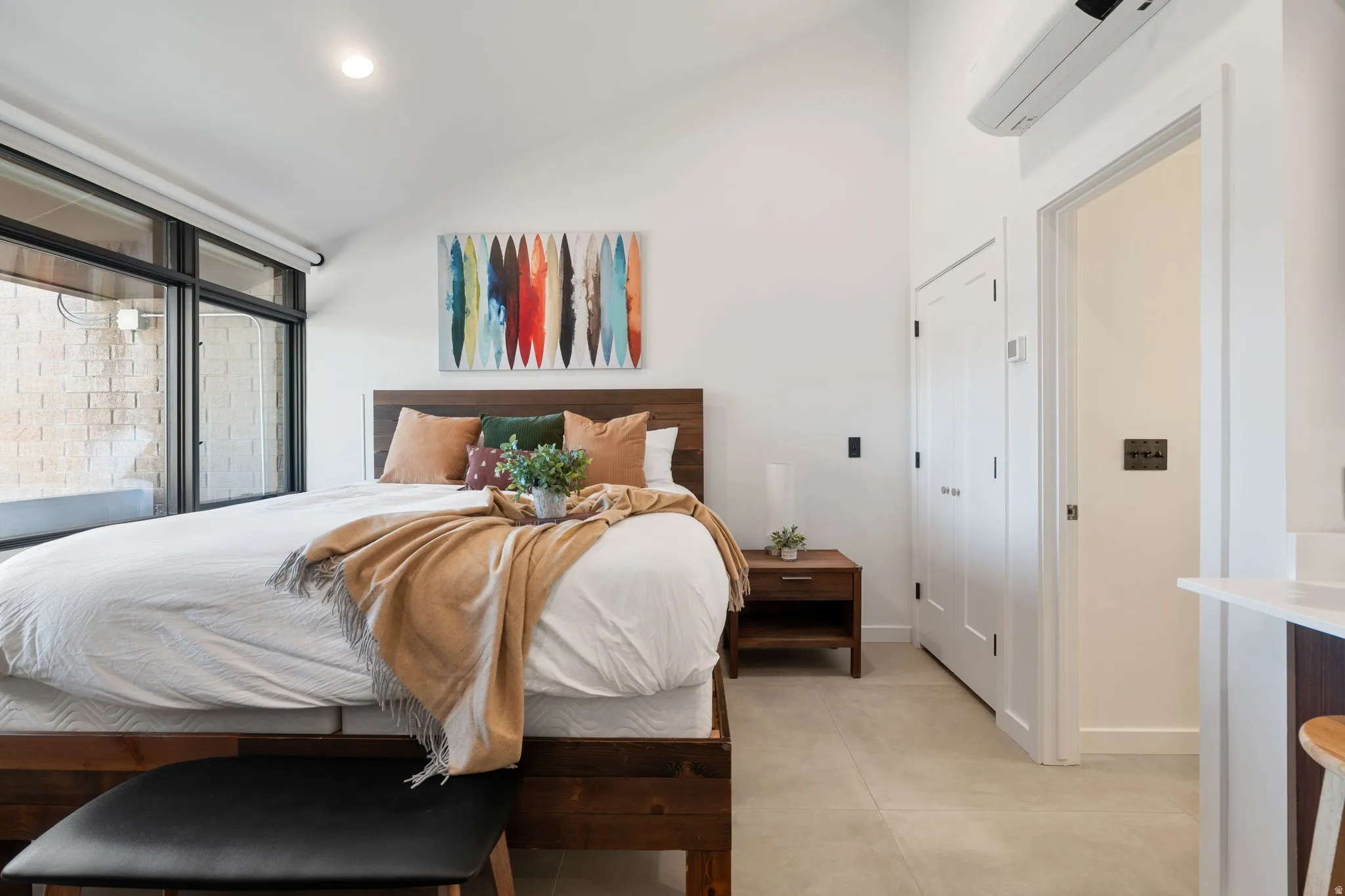 Vaulted ceiling bedroom with full-height windows, a built-in closet with double doors, wood-finish flooring, and a wall-mounted air conditioning unit
