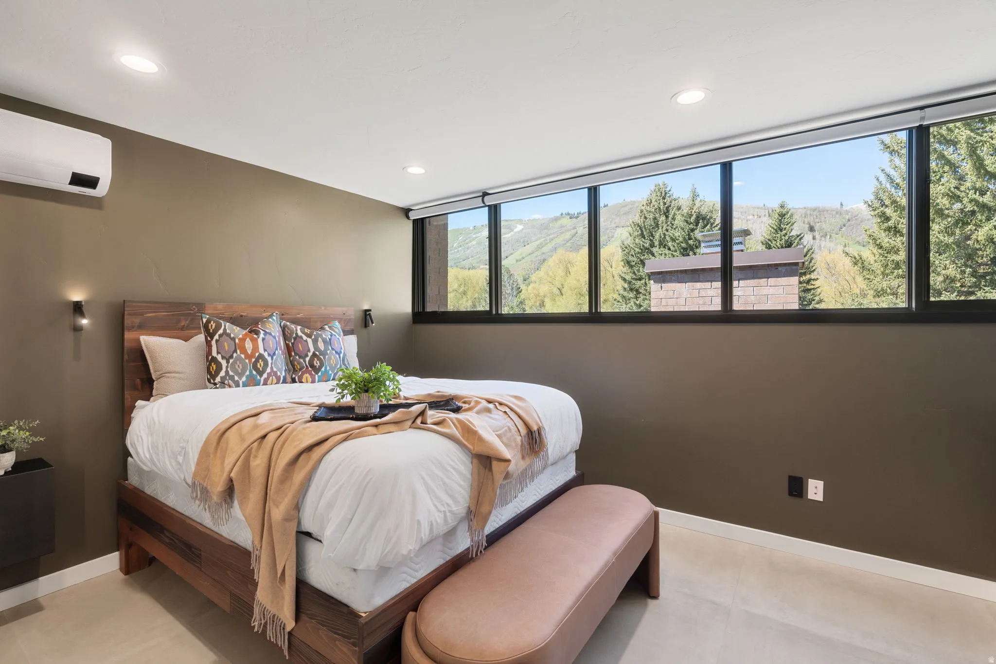 Expansive horizontal window with mountain and tree scenery, complemented by a wood-finish bed frame with a matching headboard