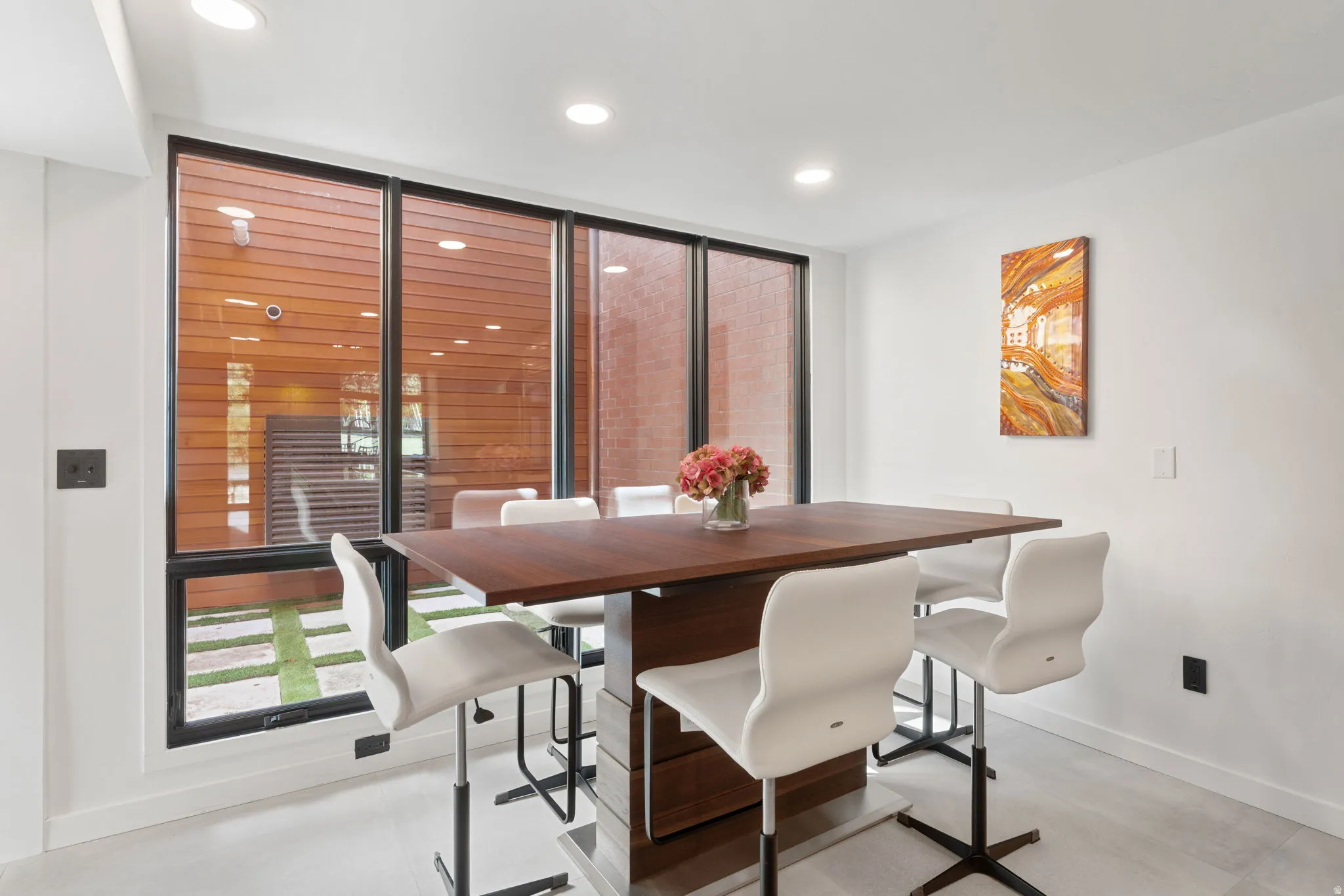 Modern dining area featuring a built-in wood-finish table with a metal base, recessed lighting, and large windows with black frames