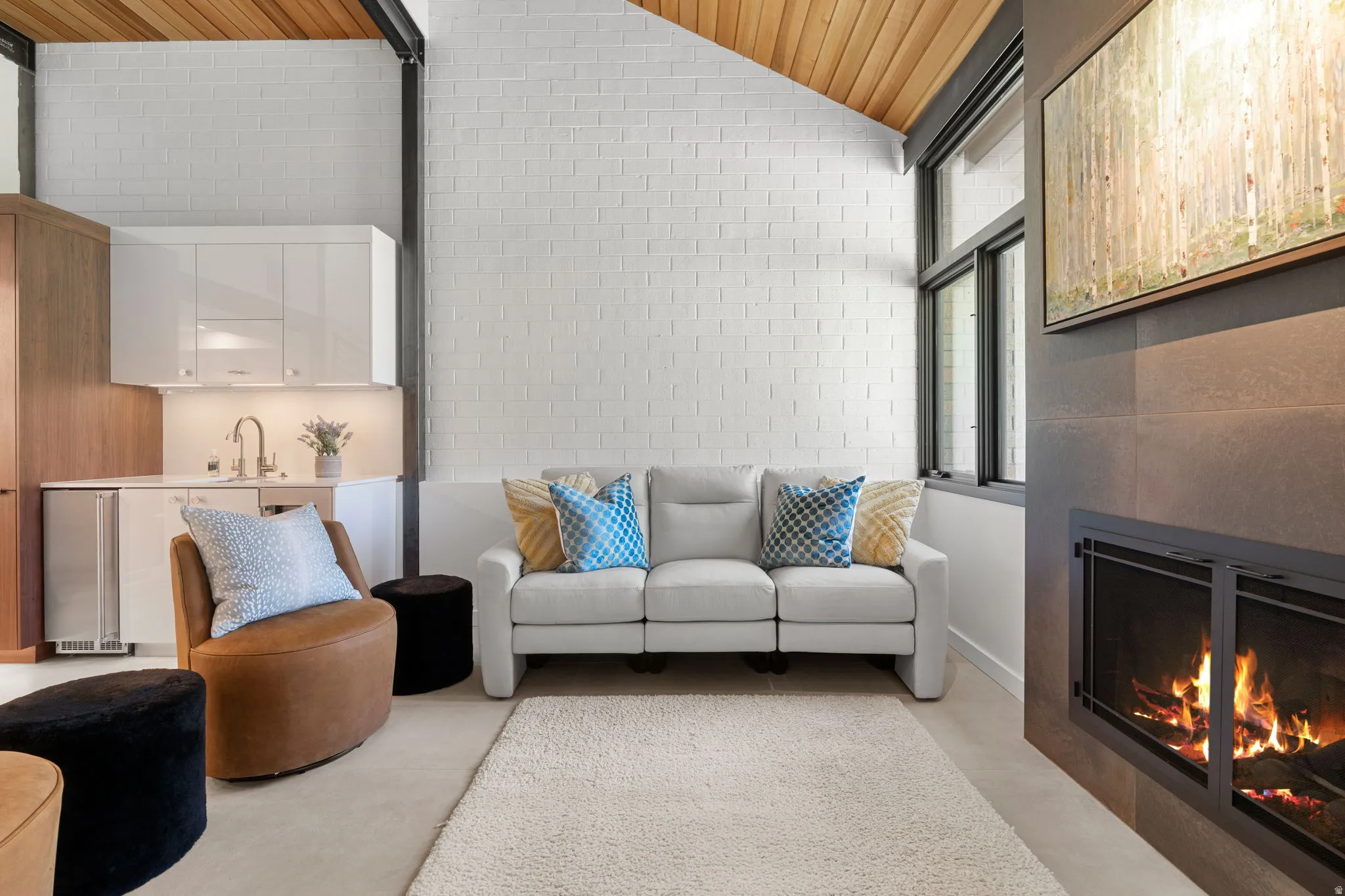 Living space featuring a natural wood-plank sloped ceiling, white brick wall, and a built-in fireplace with a dark tile surround