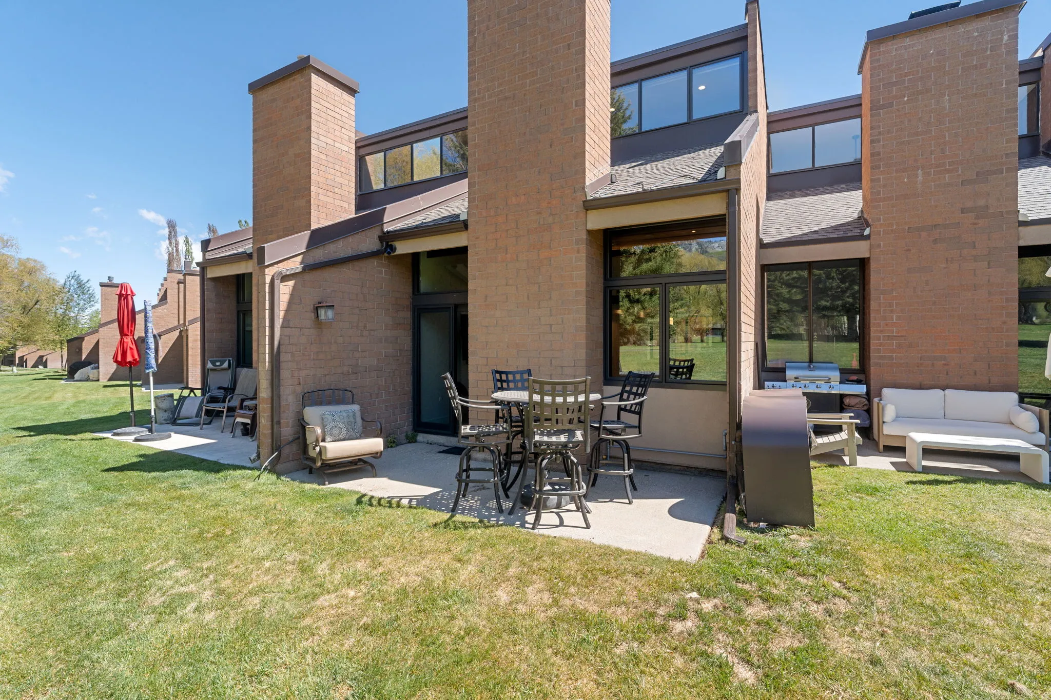 Brick exterior featuring a private concrete patio, multiple windows, and a manicured lawn