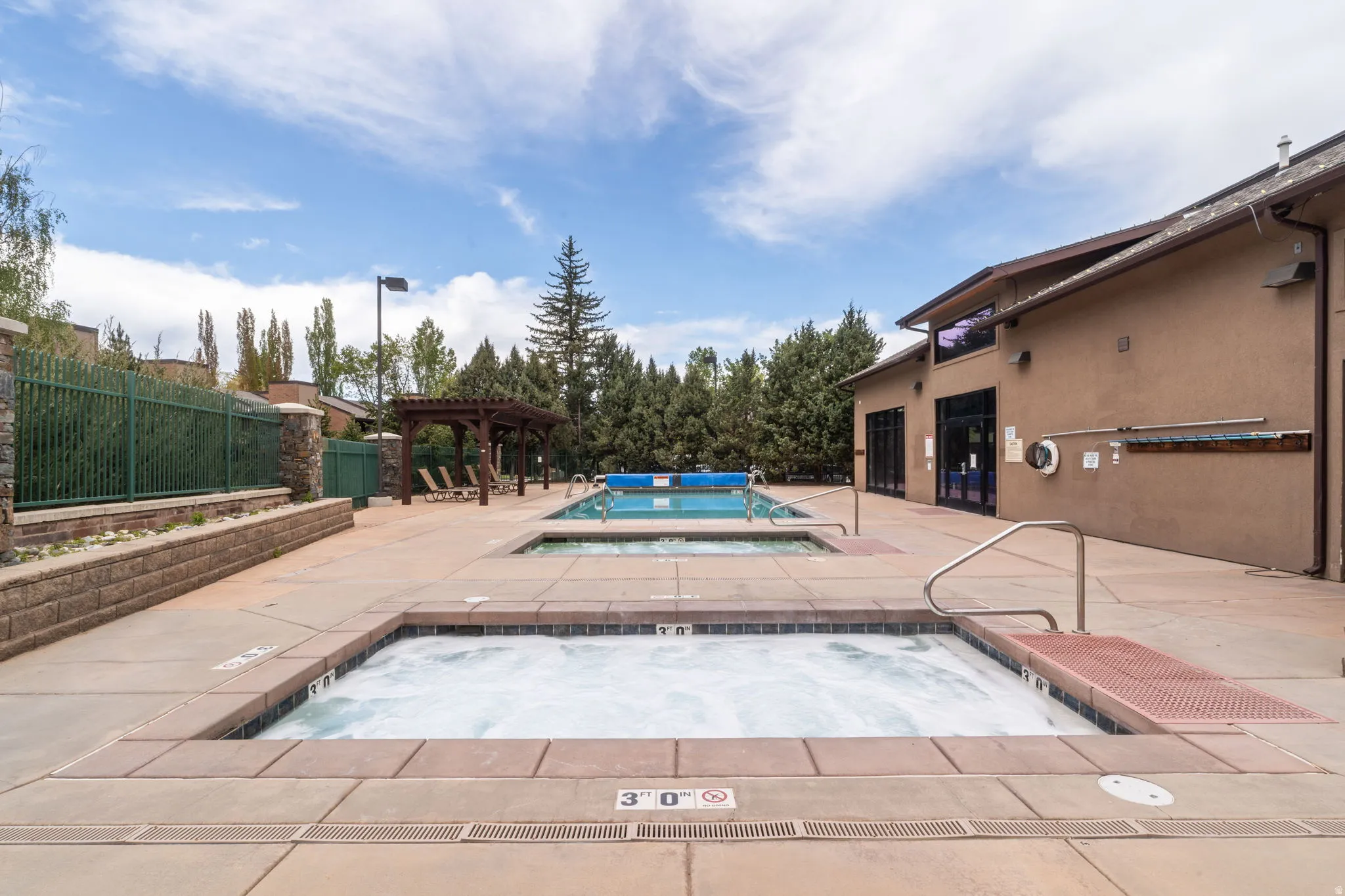 Outdoor amenity area featuring a hot tub, two pools, and a wooden pergola