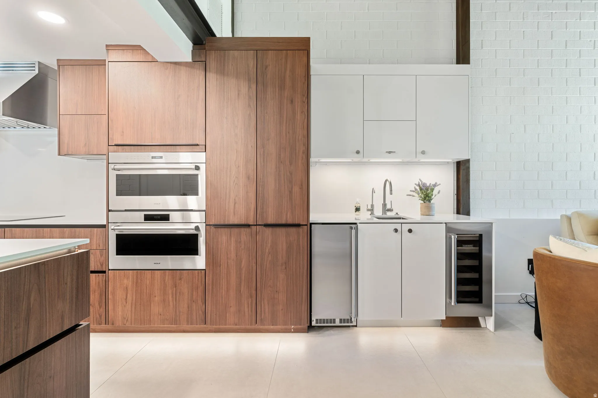 Contemporary kitchen and wet bar featuring wood-finish cabinetry, integrated stainless steel appliances, a beverage cooler, white countertops, and a subway tile backsplash