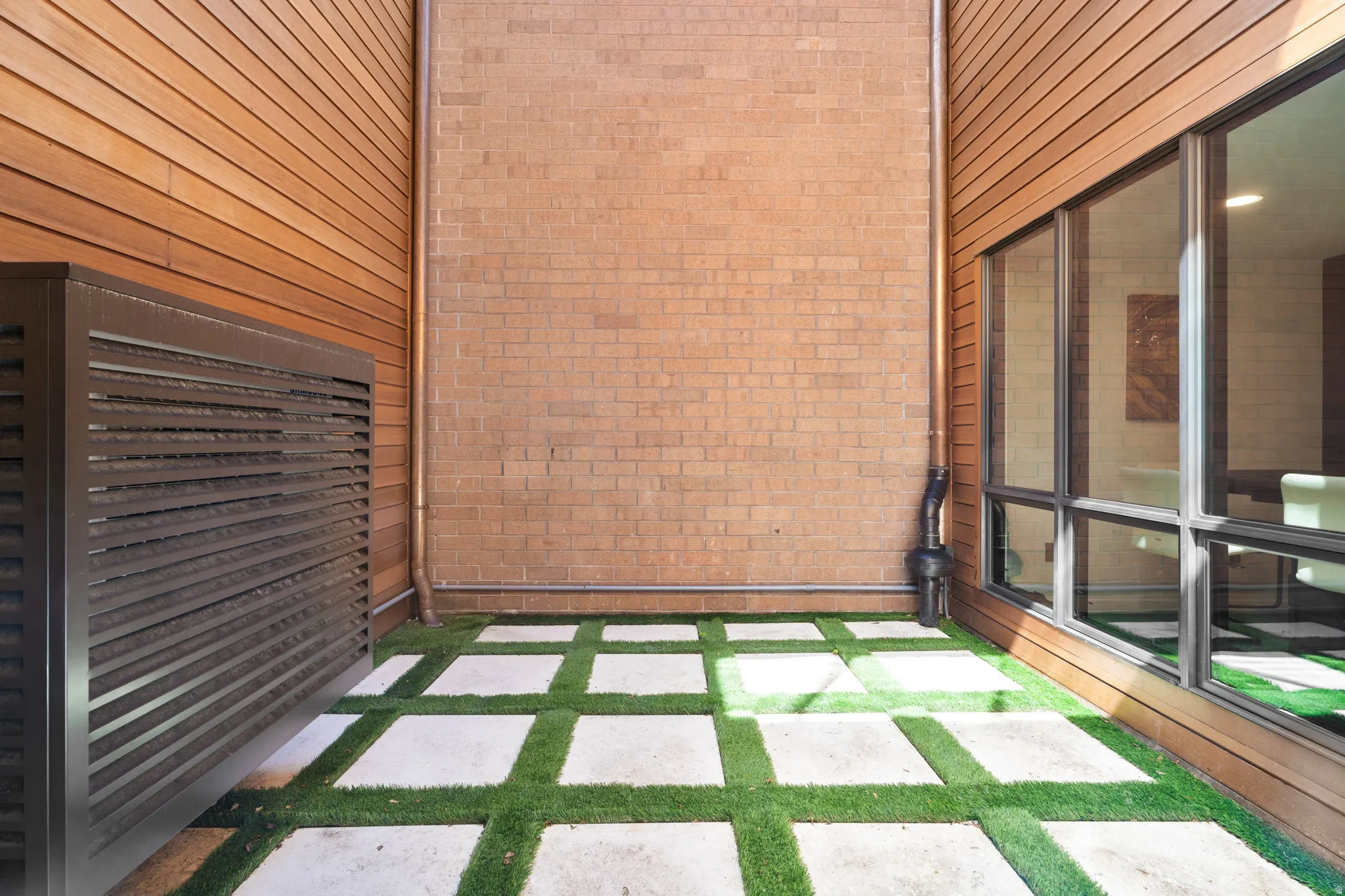 Outdoor courtyard featuring artificial turf with square pavers, brick wall, and horizontal wood siding