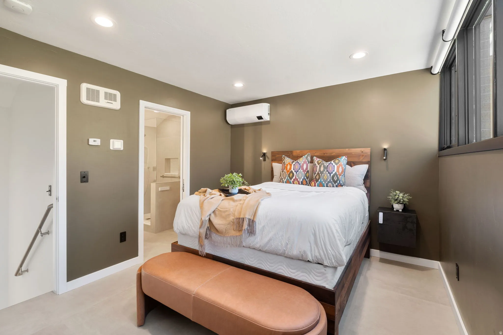 Neutral-toned bedroom featuring recessed ceiling lighting, a wall-mounted mini-split system, and light-colored flooring