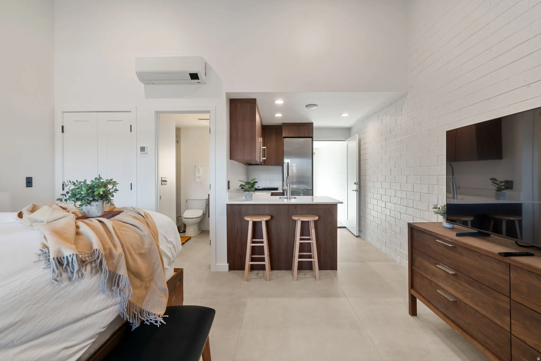 Bright open-concept living space with a modern kitchen, featuring wood-finish cabinetry, a white countertop island, and stainless steel appliances