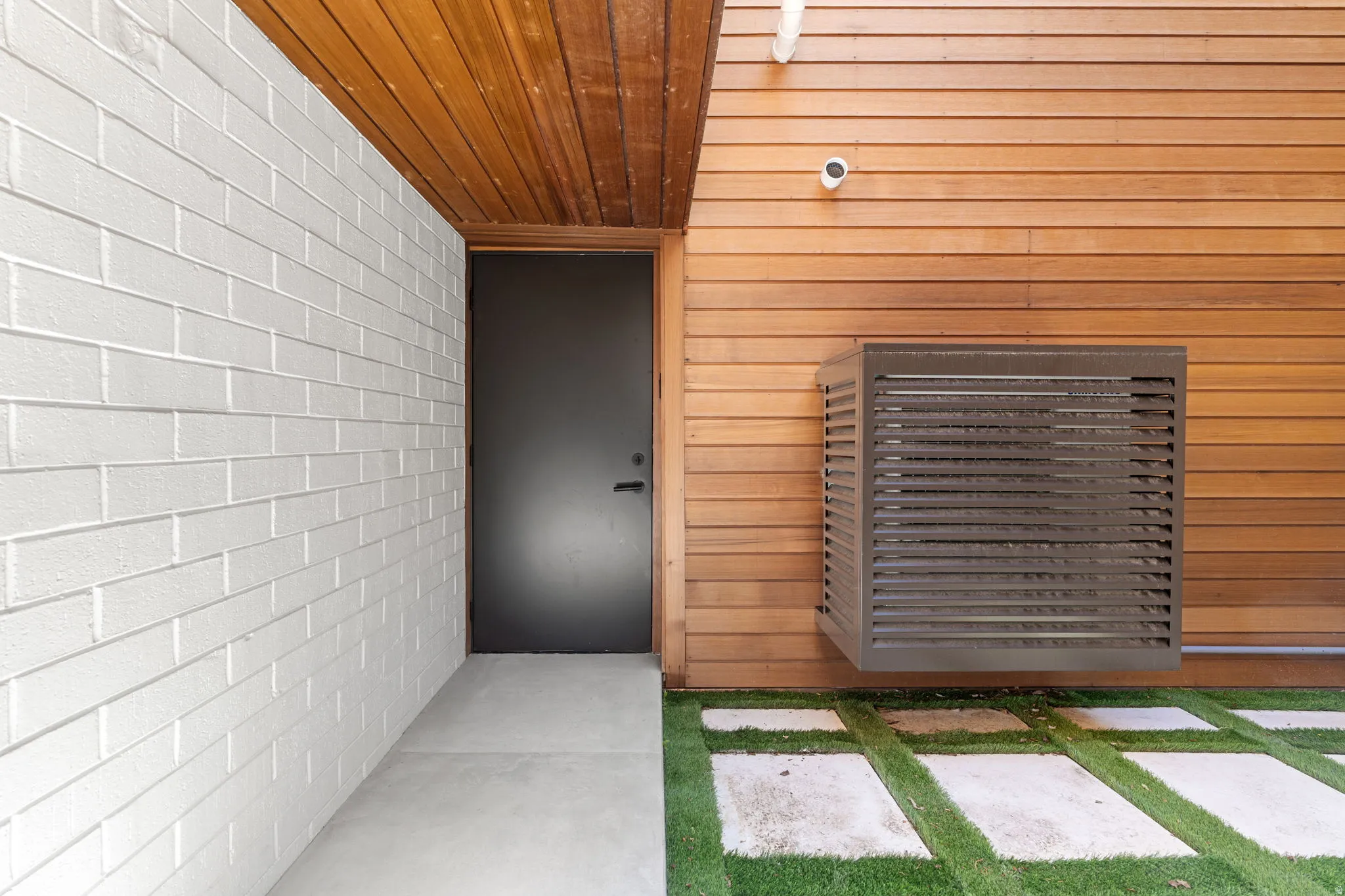 Modern exterior featuring wood-panel siding, a white brick wall, and a dark entry door