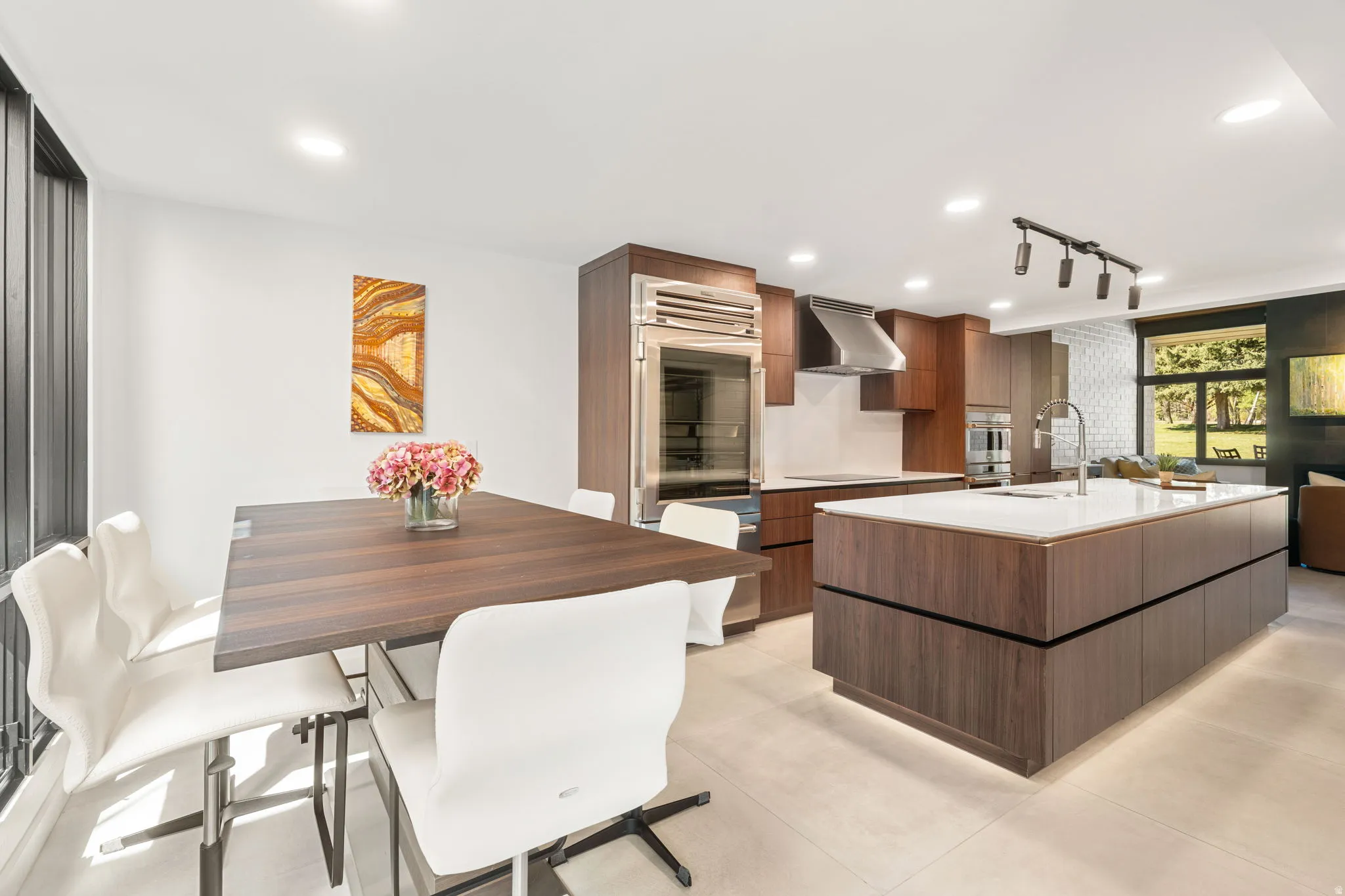 Open-concept kitchen and dining area featuring a large center island with integrated sink, stainless steel appliances, dark wood-finish cabinetry, and recessed lighting