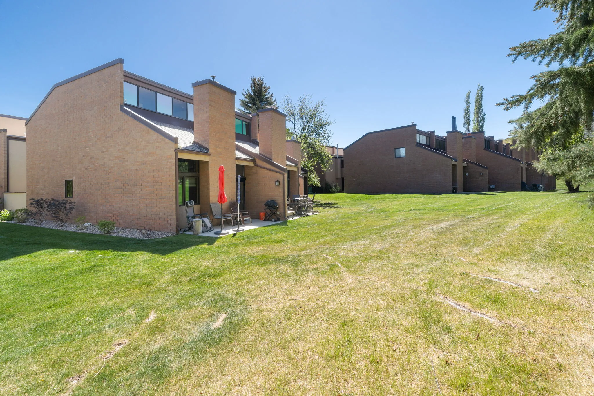 Brick townhouse exterior with multiple windows, a rear patio, and a sloped roofline