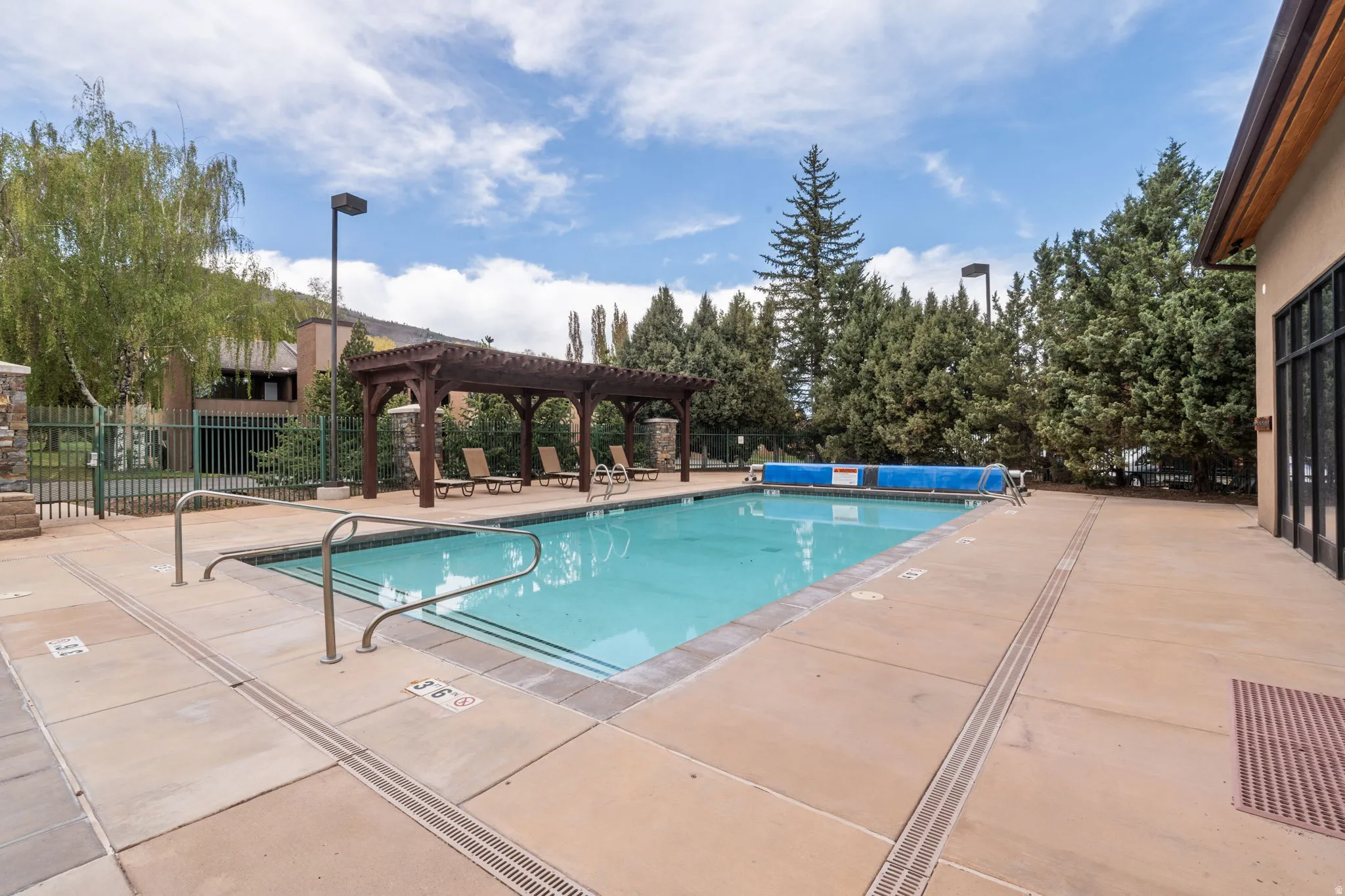 Outdoor swimming pool with concrete decking, a wooden pergola, and perimeter landscaping