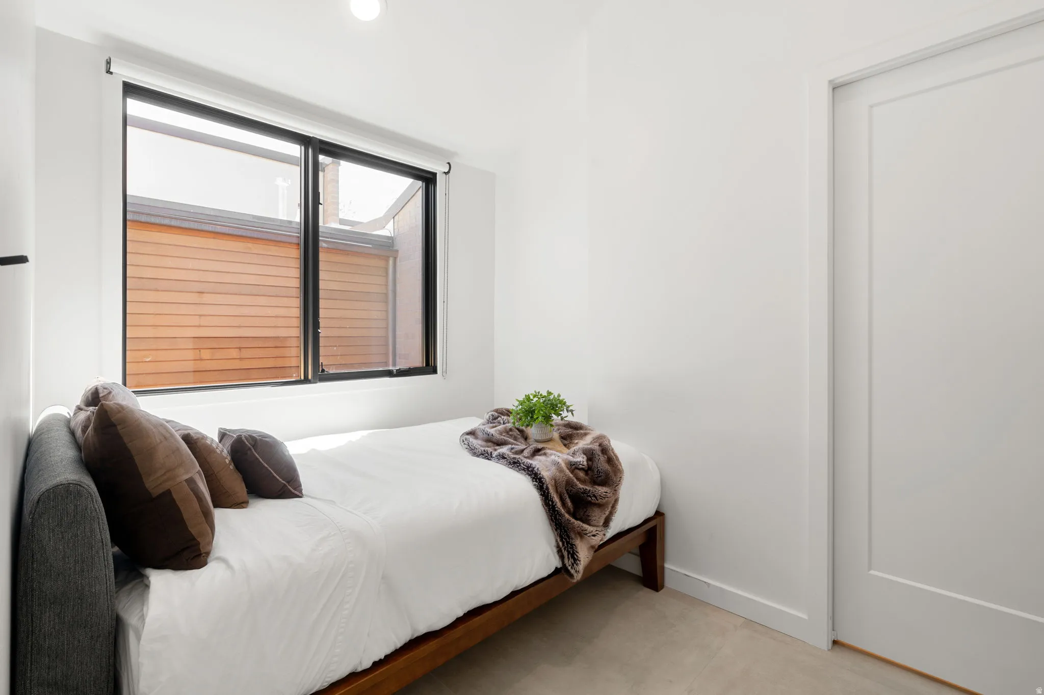 White walls, a single window with black trim, and a flush-panel door define this room