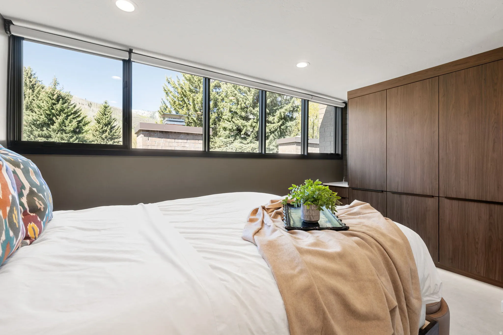 Expansive window wall with mountain and tree scenery, complemented by recessed lighting and full-height built-in wood-finish cabinetry