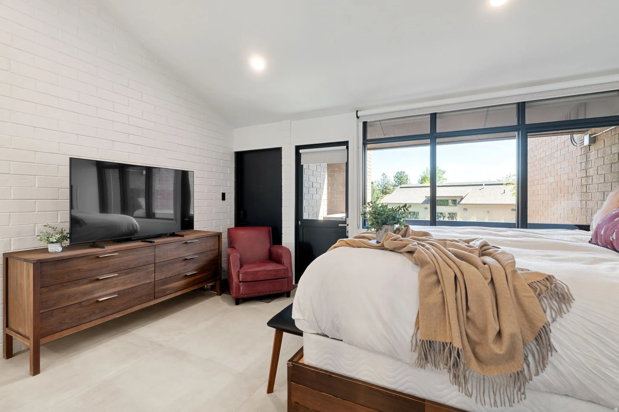 Bedroom featuring a vaulted ceiling with recessed lighting, whitewashed brick accent wall, and wood-finish flooring