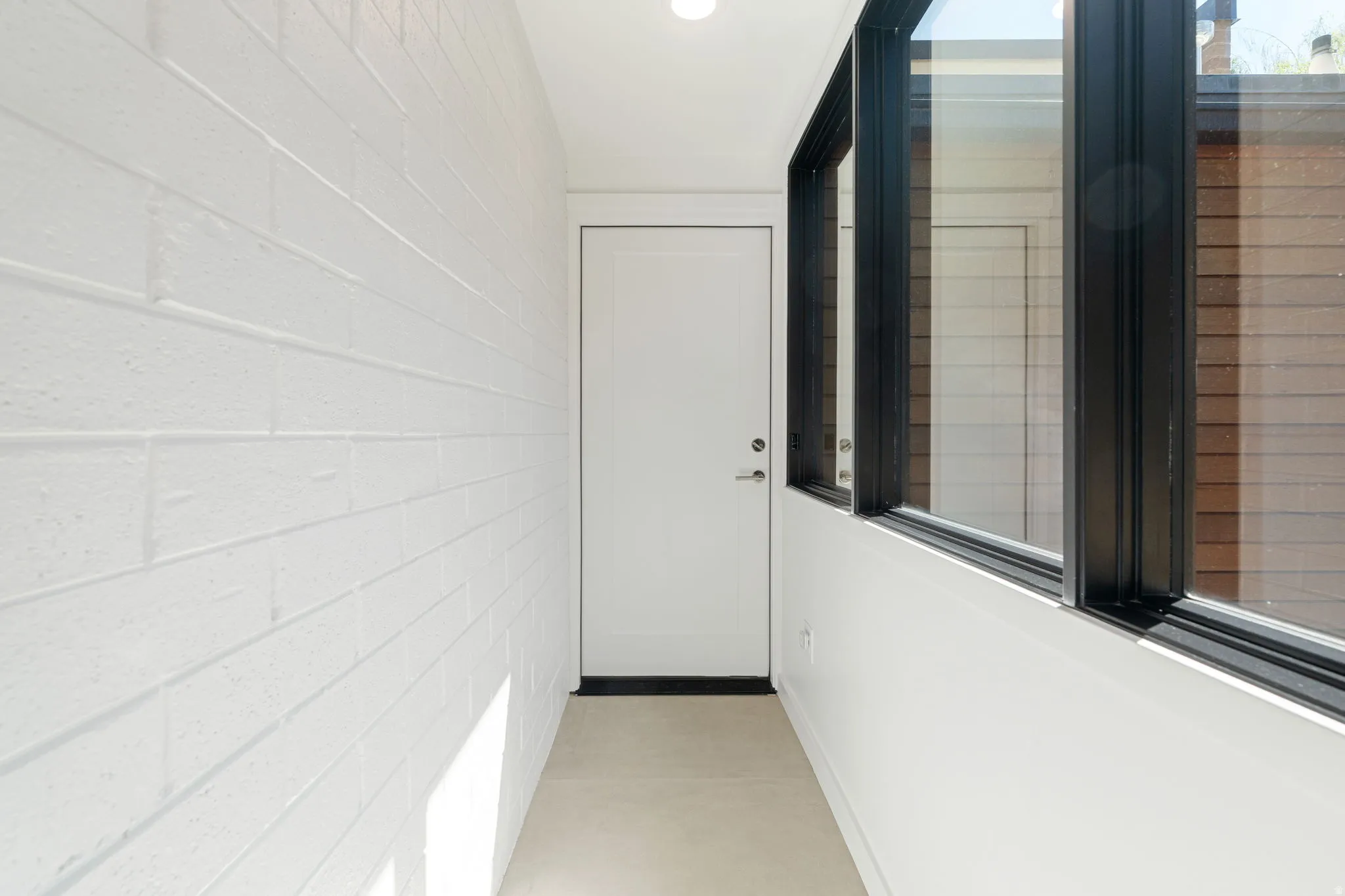 Entryway featuring a white door with dark hardware, a light-colored floor, and a white brick-textured wall