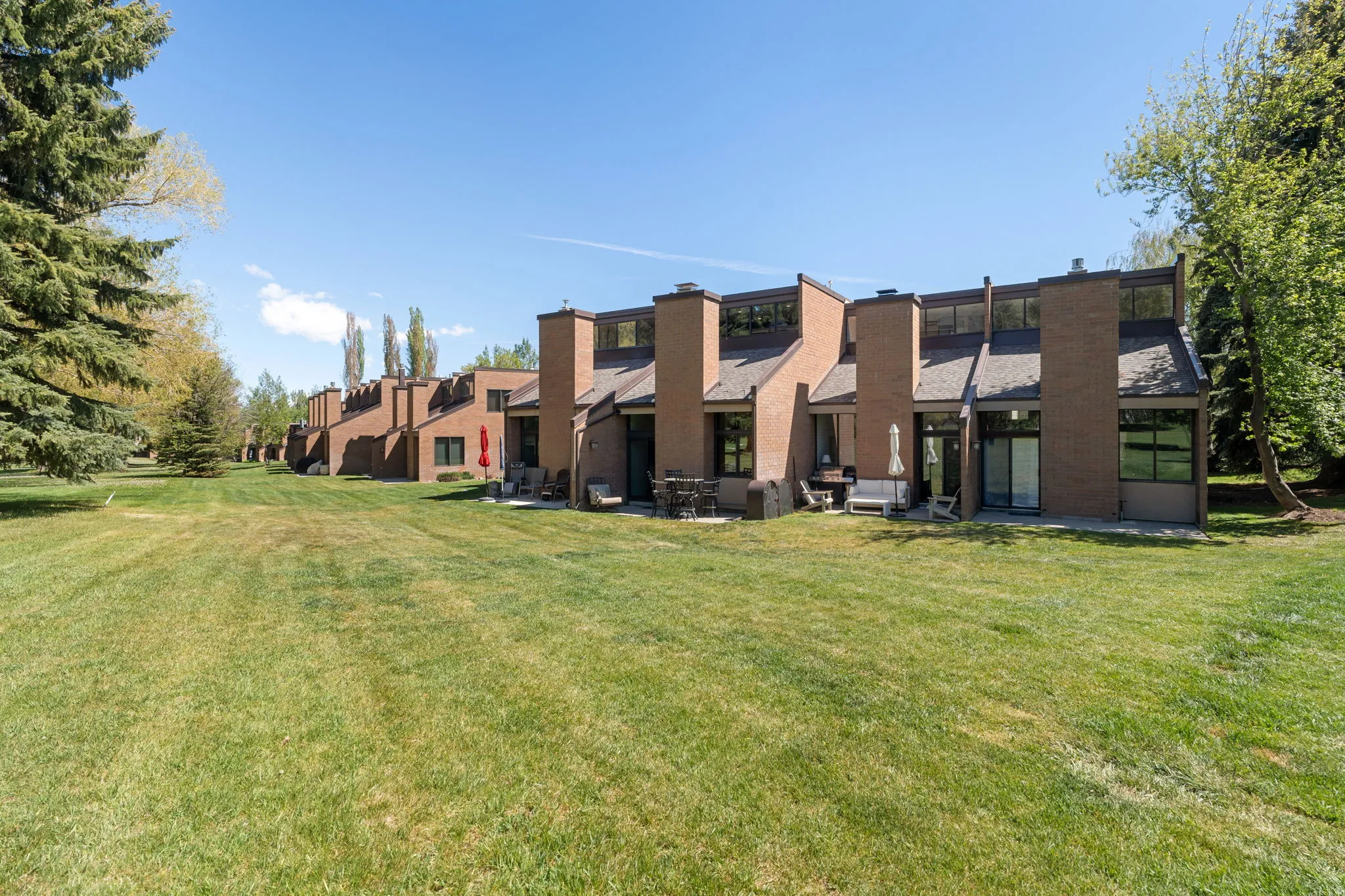 Expansive green lawn bordering brick townhome-style residences featuring private patios, upper-level windows, and mature trees