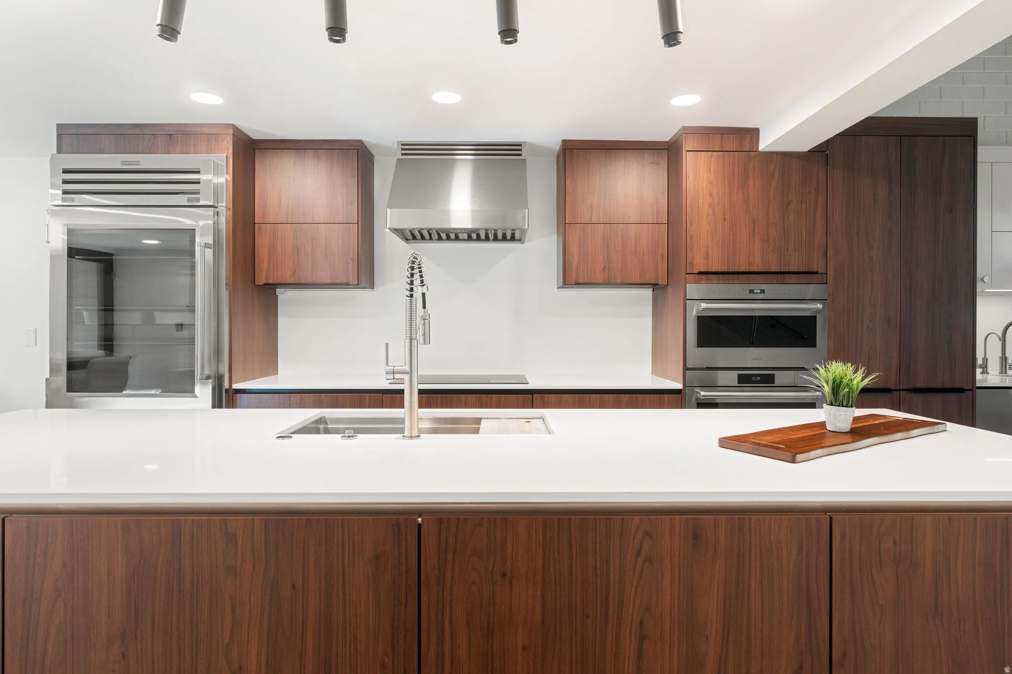 Kitchen featuring a large island with an undermount sink, white countertops, rich wood-finish cabinetry, stainless steel appliances, and recessed lighting