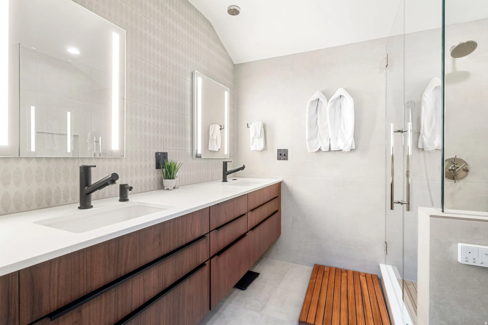 Dual vanity with integrated sinks, matte black fixtures, backlit mirrors, and rich wood-finish cabinetry