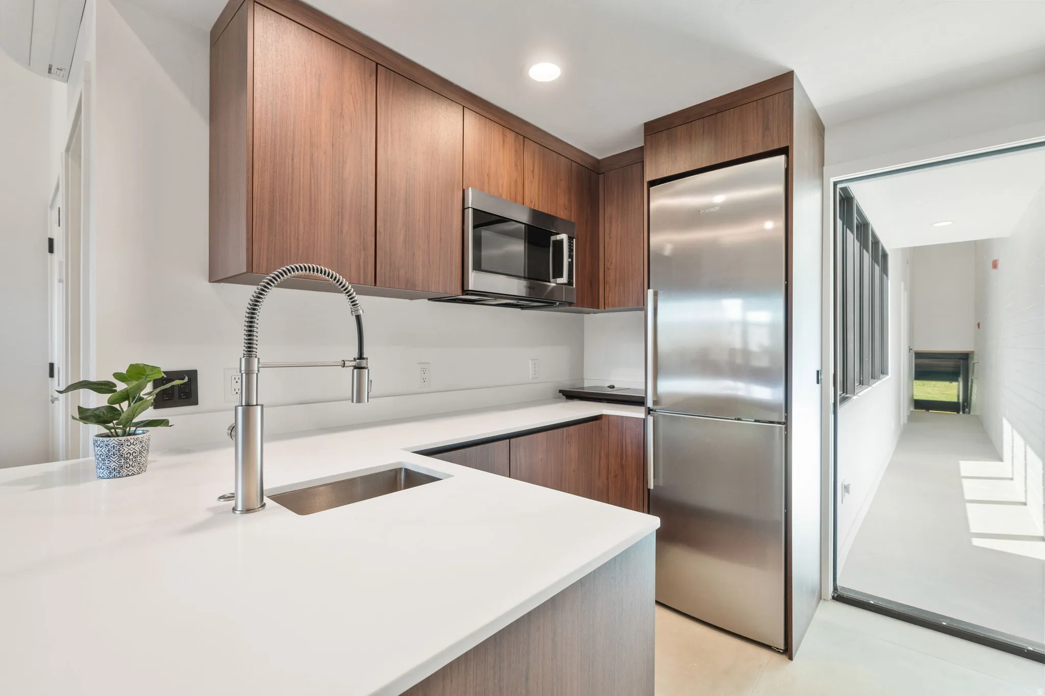 Modern kitchen featuring wood-finish cabinetry, stainless steel appliances, a pull-down faucet, and white countertops