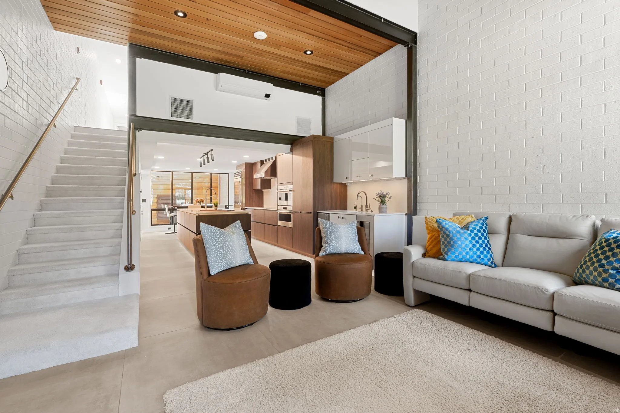 Open-concept living space featuring a white brick accent wall, light wood-finish ceiling, and integrated kitchen with a built-in wet bar