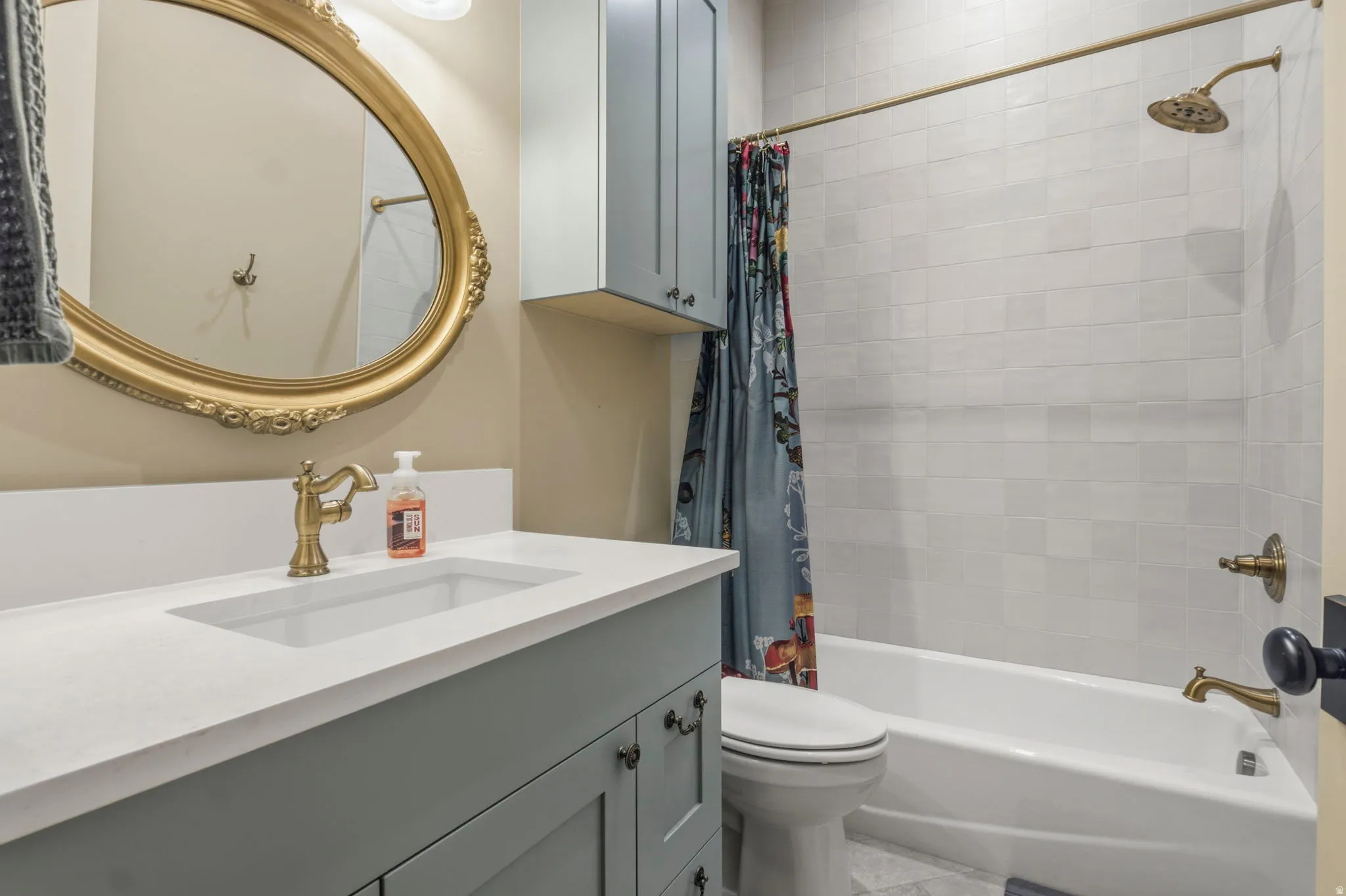 Bathroom featuring a light blue vanity with a white countertop and integrated sink, an ornate gold-framed mirror, a bathtub with subway tile surround, and coordinating brass fixtures