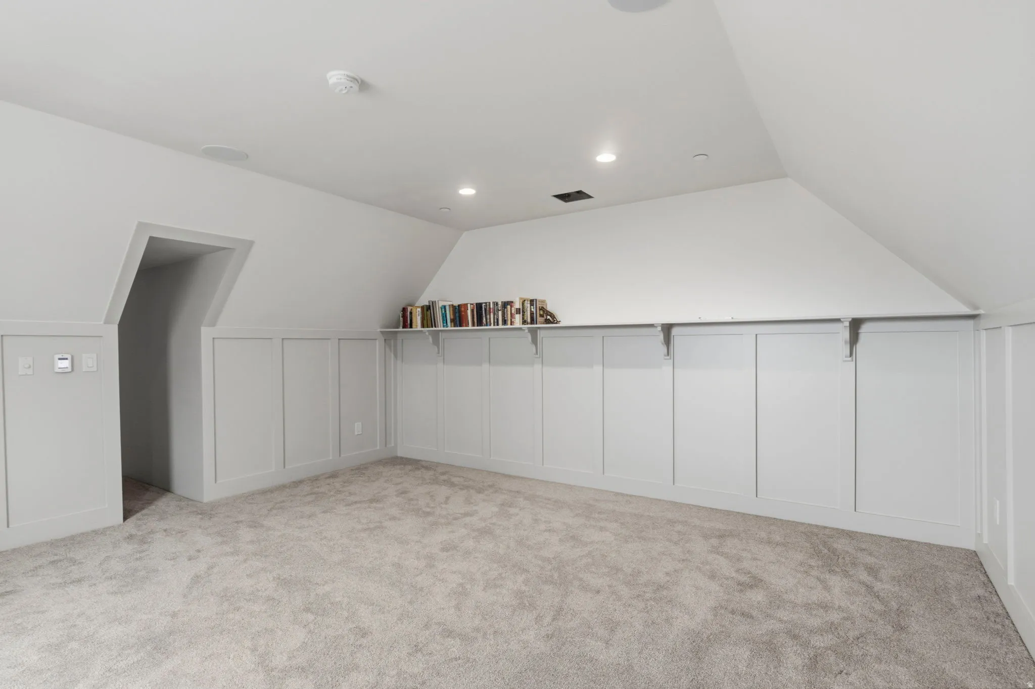 Carpeted Quiet room off the attic area behind a hidden door with sloped ceilings, recessed lighting, and integrated wall shelving