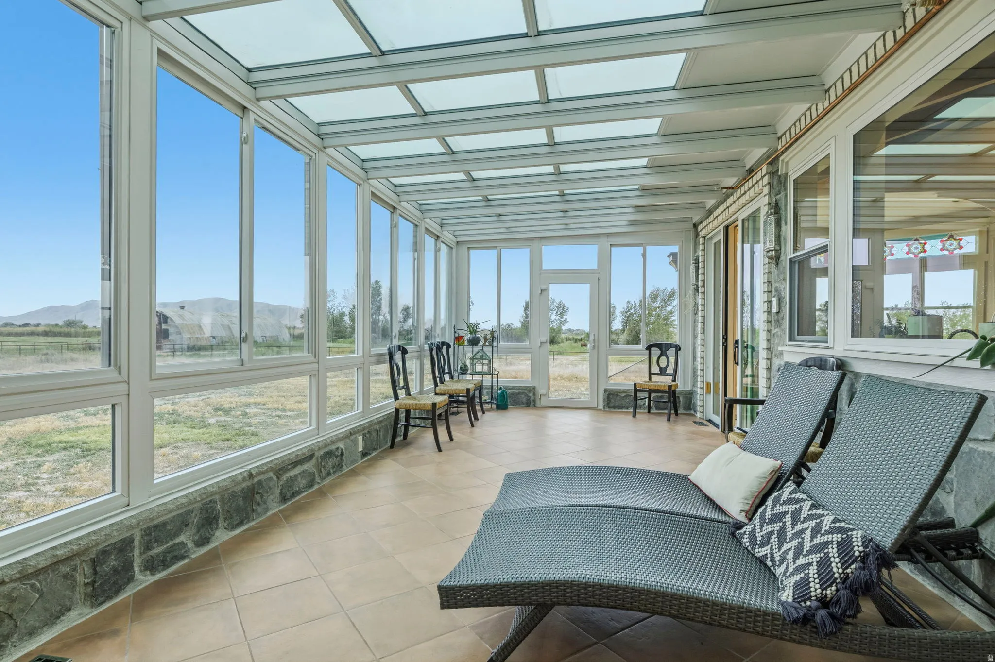 Solarium Sunroom featuring a full glass roof, floor-to-ceiling windows, stone base, tile flooring, and exterior access for enjoying nature in style.