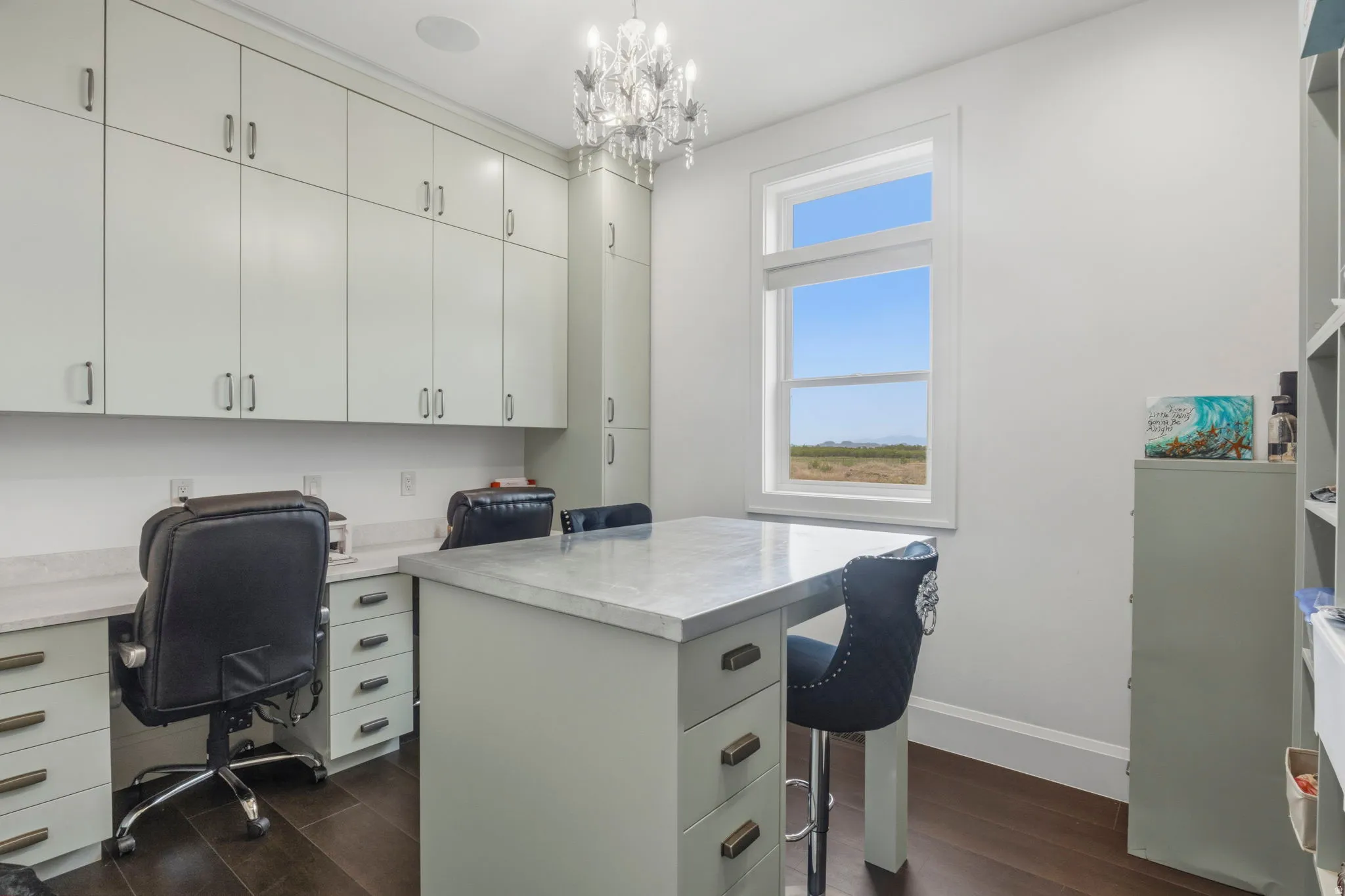 Craft room or Dedicated workspace featuring extensive built-in cabinetry, dual workstations with light-toned countertops, a central island with a contrasting countertop, and dark wood-finish flooring