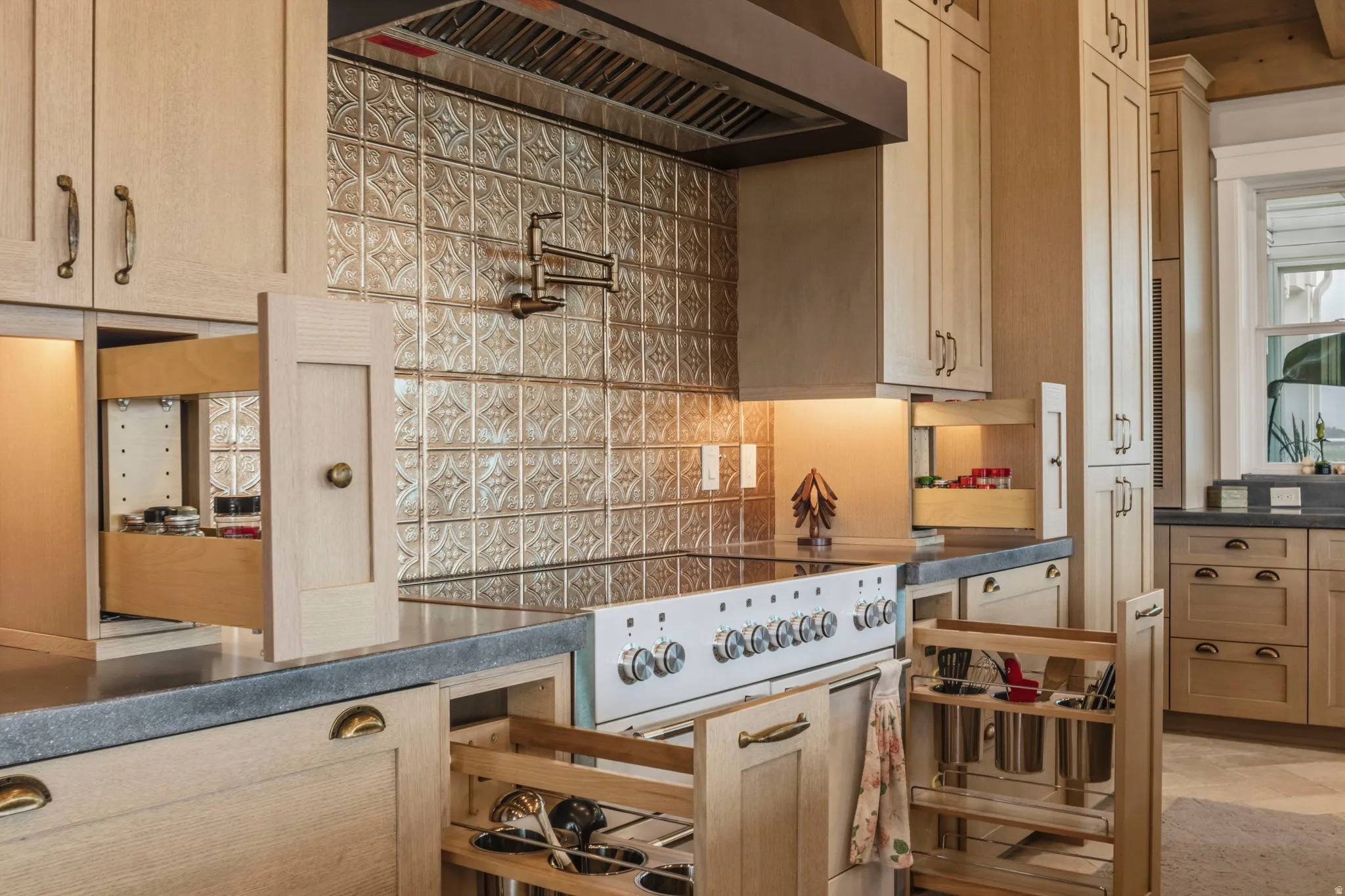 Kitchen featuring a detailed tile backsplash, stainless steel range hood, and a pot filler, utensil drawers and spice racks