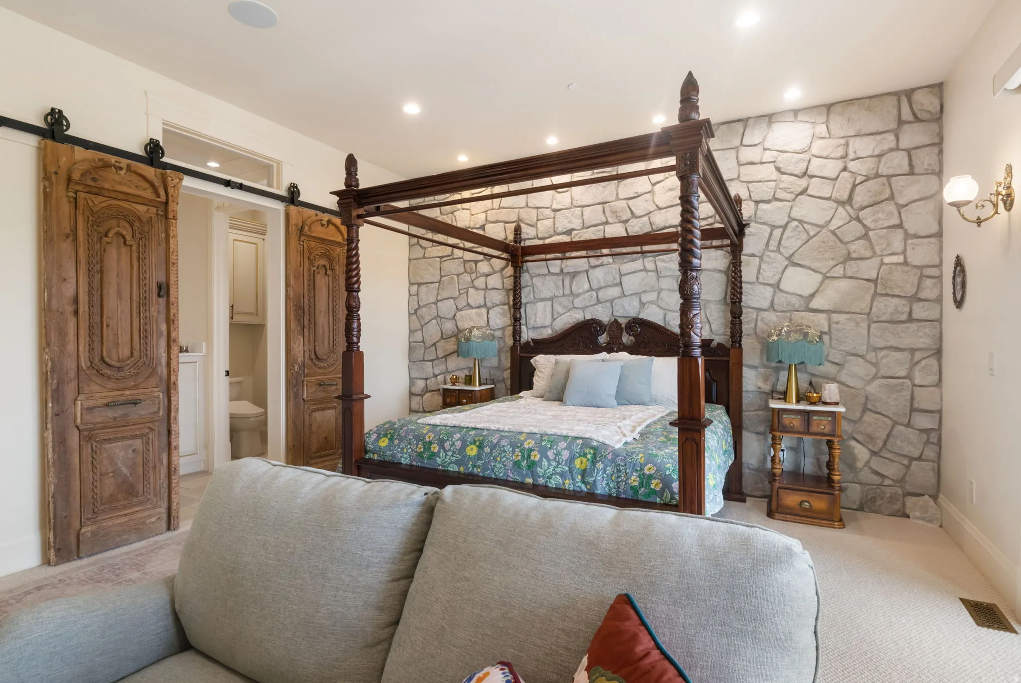 Stone accent wall with recessed lighting, complemented by dual barn doors with carved wood panels and black iron hardware, and wall-mounted sconces