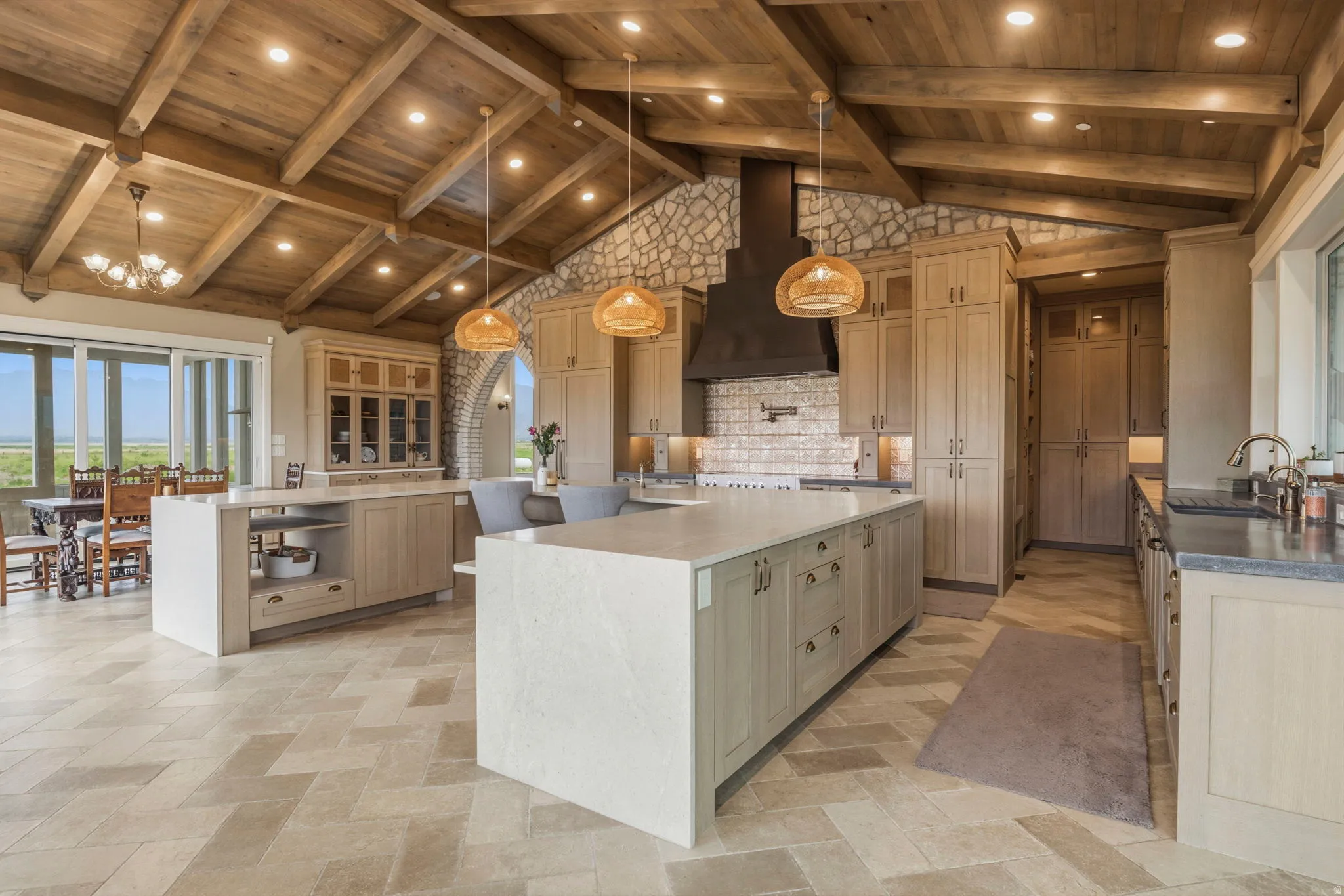 Spacious kitchen featuring exposed wood beam vaulted ceilings, stone accent walls, dual islands with light-toned countertops, extensive cabinetry, and herringbone pattern tile flooring
