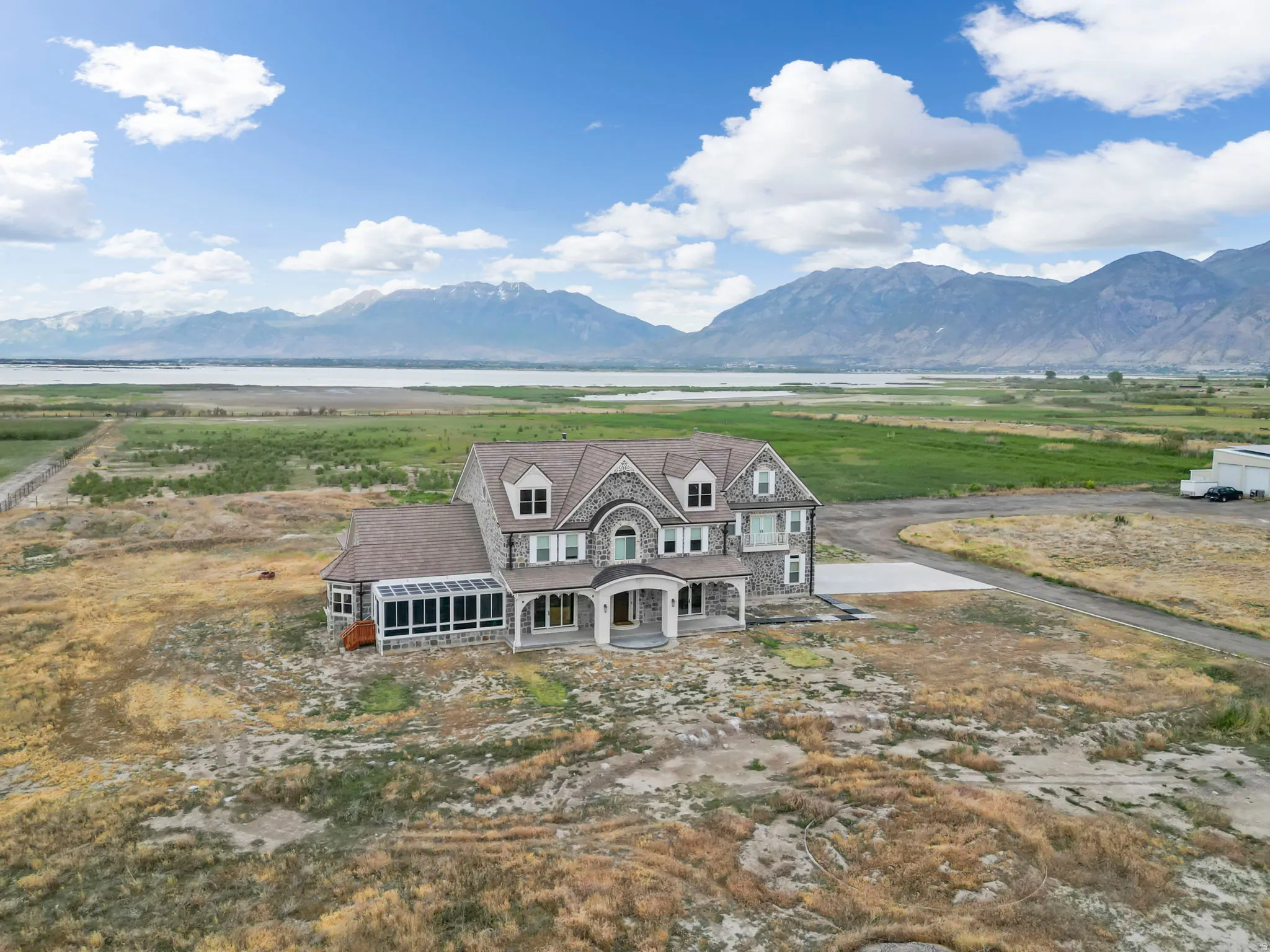 Stone facade residence featuring a covered entry porch, multiple gables, a sunroom with extensive windows, and a paved driveway leading to the property