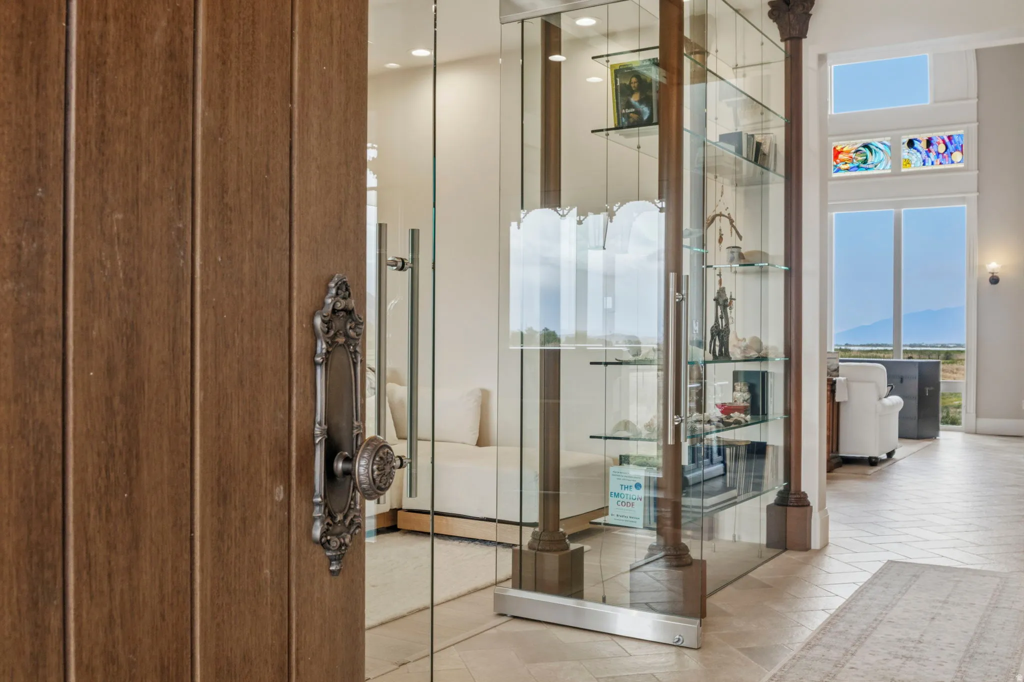 Entryway featuring a wood-finish door with ornate hardware, glass partition walls, integrated display shelving, and tall windows providing abundant natural light