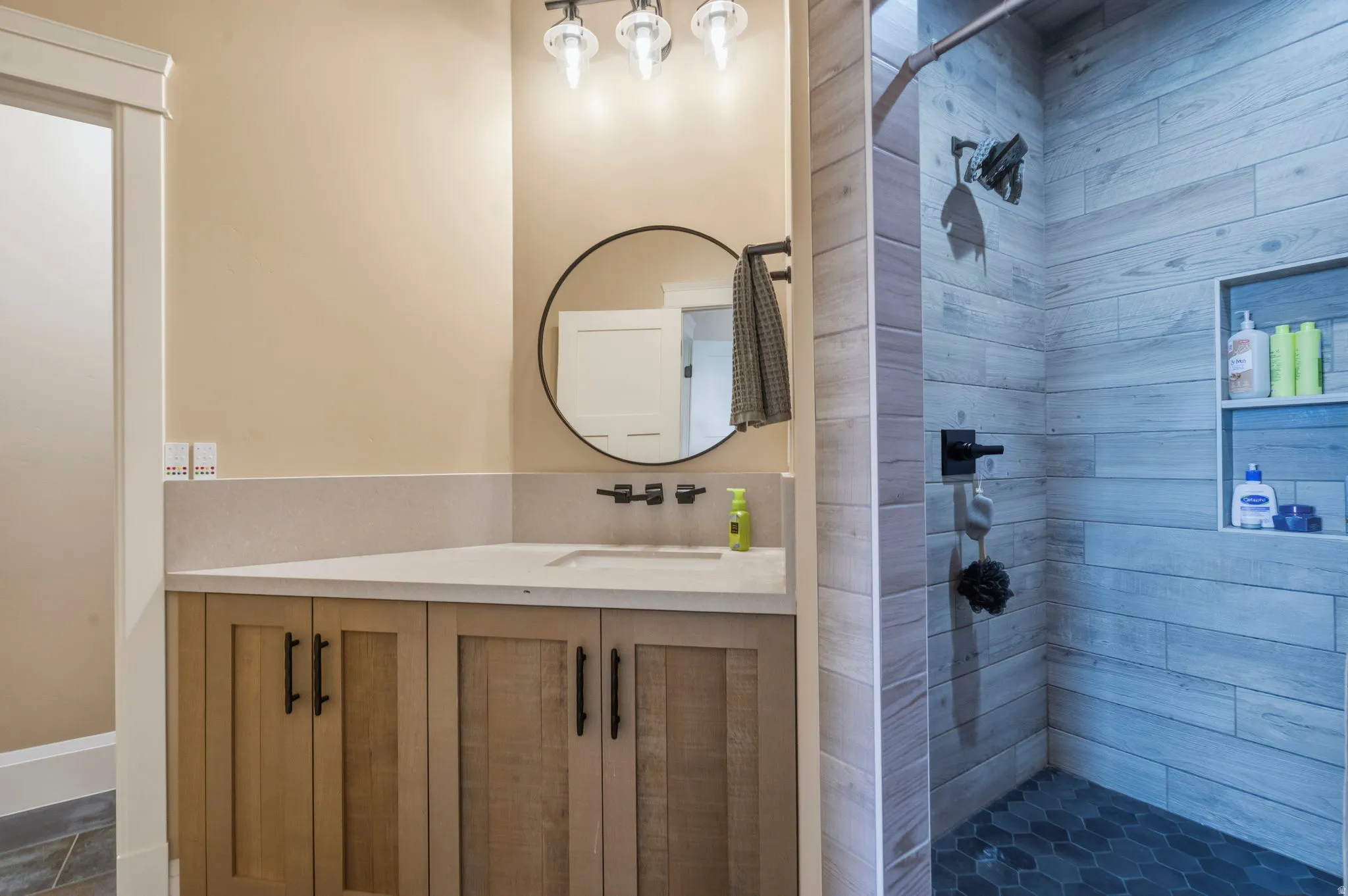 Bathroom featuring a light wood-finish vanity with a light-toned countertop, a round black-framed mirror, and a black wall-mounted faucet