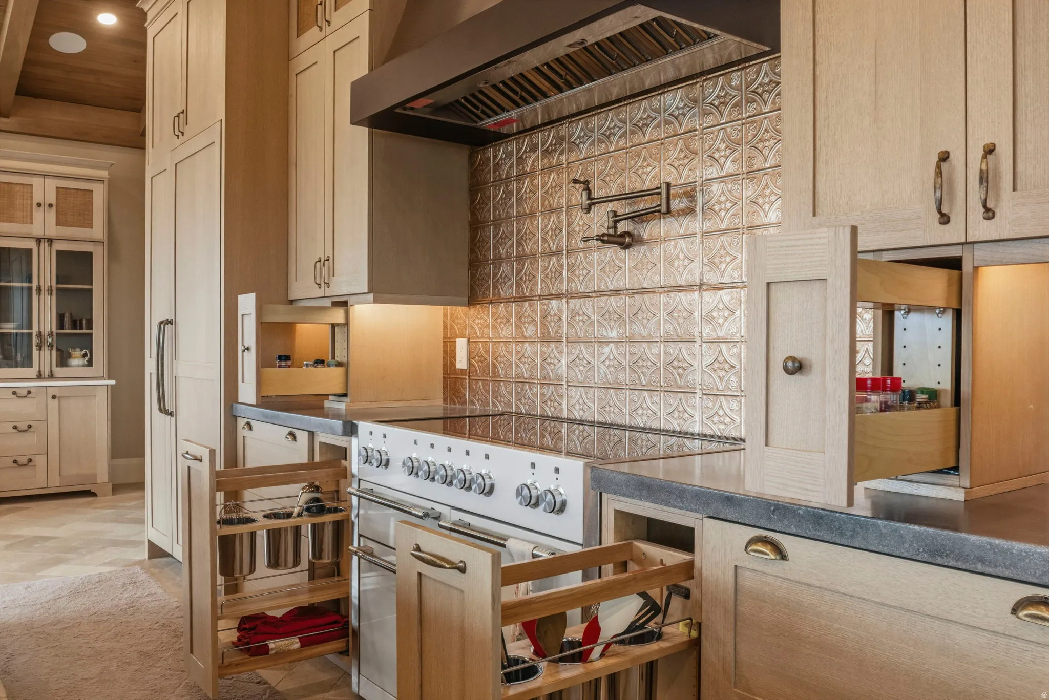 Gourmet kitchen featuring a professional-grade range, ornate tile backsplash, integrated range hood, solid surface countertops, and custom cabinetry with pull-out organizers