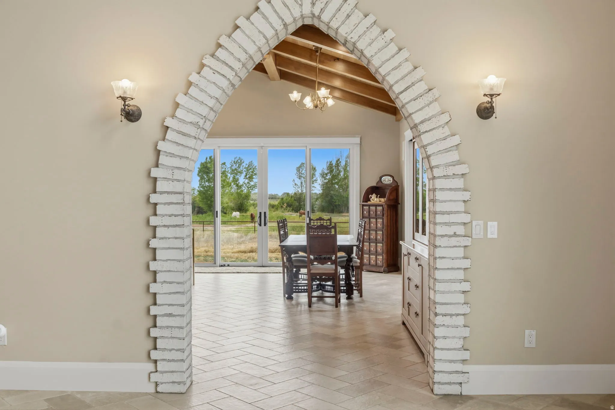 Brick archway entry to Kitchen featuring sconce lighting, herringbone flooring, vaulted ceiling with exposed beams, and sliding glass doors to outdoor spaces