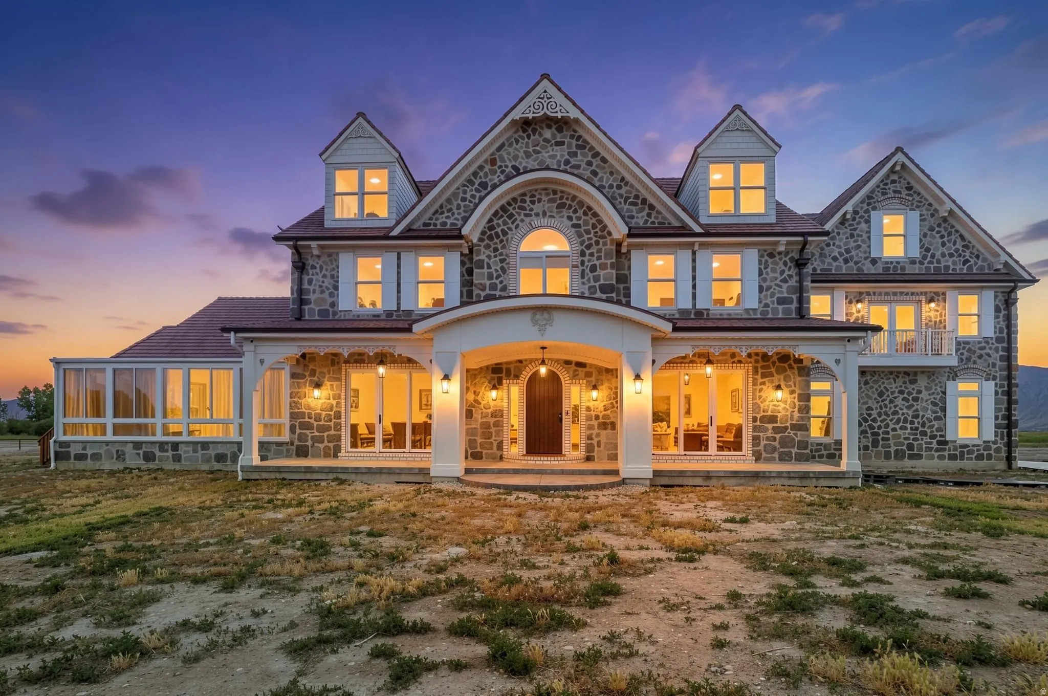 Stone-clad exterior featuring multiple dormers, a covered porch with white columns, and a sunroom extension