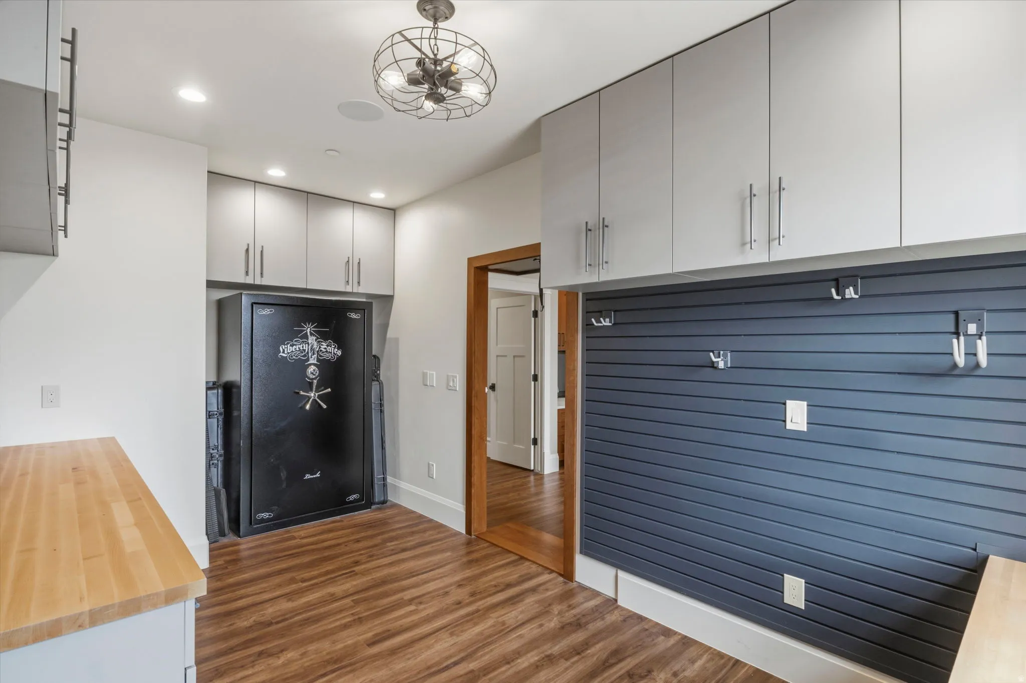 Secret workshop/Utility space featuring wood-finish flooring, light gray cabinetry, and a dark blue slatwall system with hooks