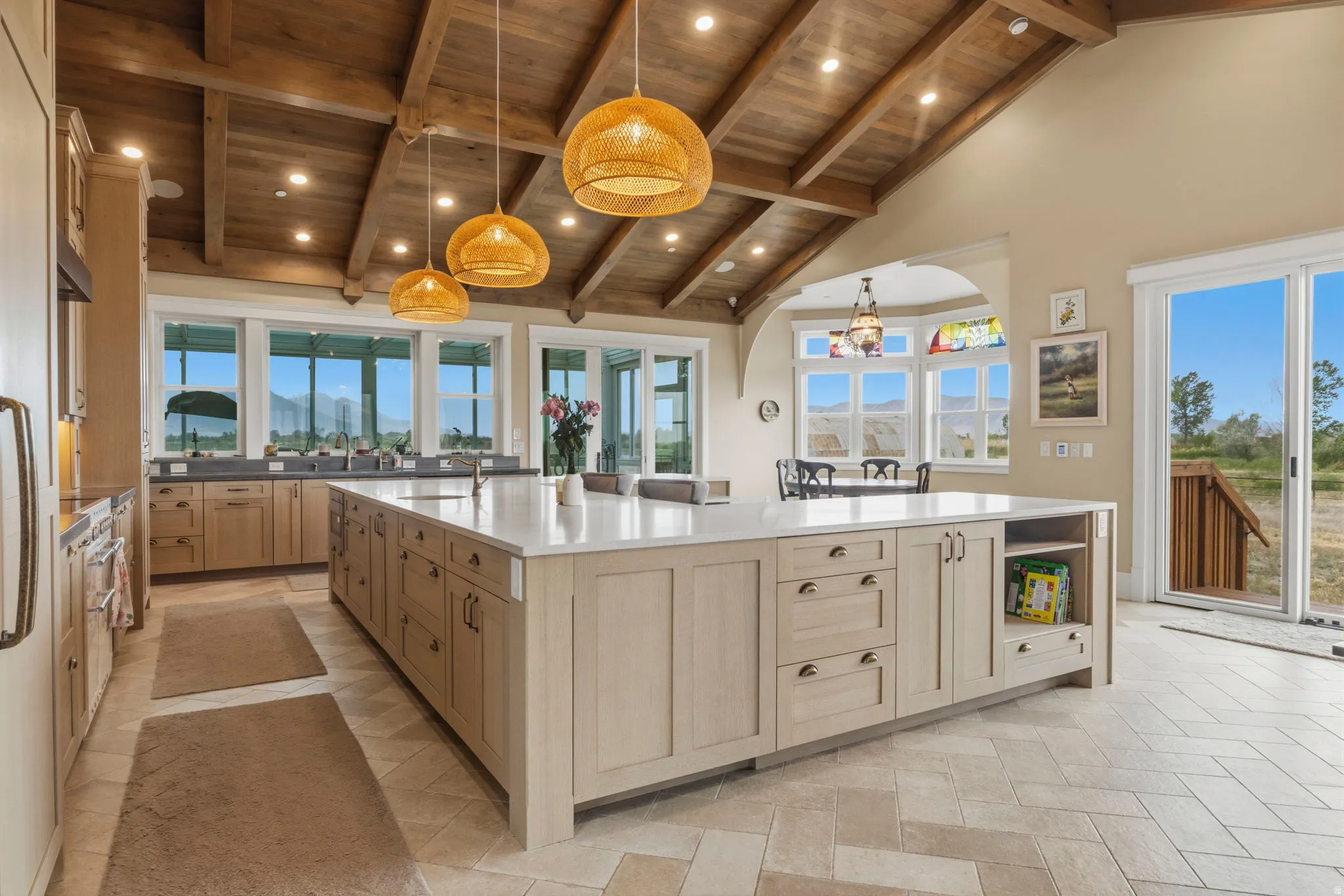 Gourmet kitchen featuring a substantial central island with a solid surface countertop, abundant light-toned cabinetry, and a vaulted wood-plank ceiling with exposed beams
