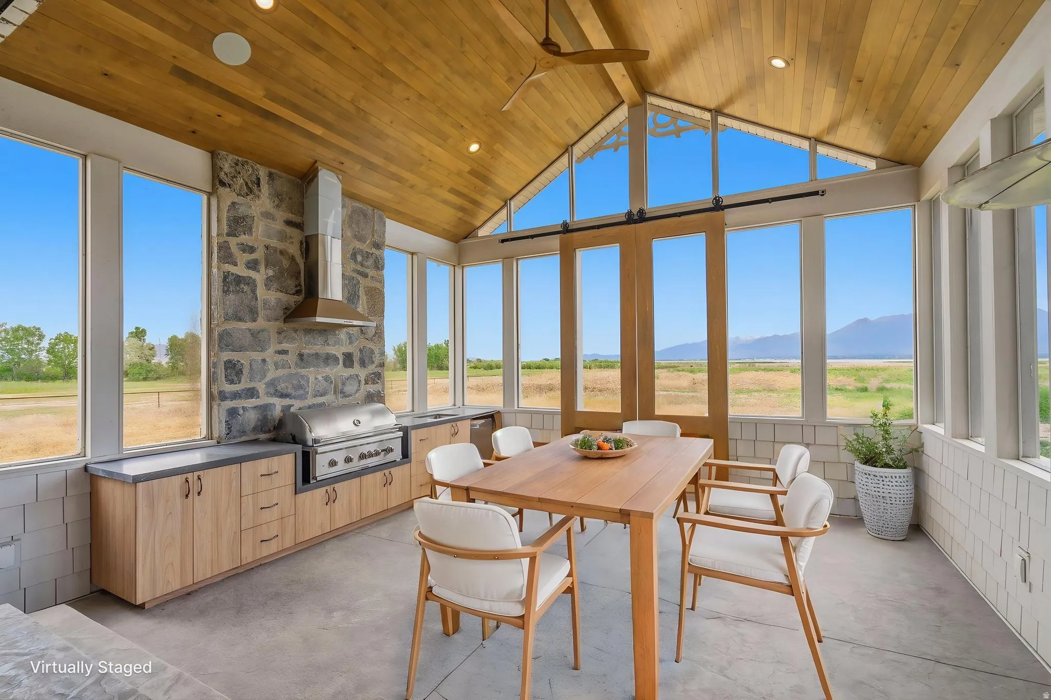 Expansive outdoor living area featuring a vaulted wood-finish ceiling, stone accent wall with built-in grill and range hood, full-height windows, and sliding glass doors