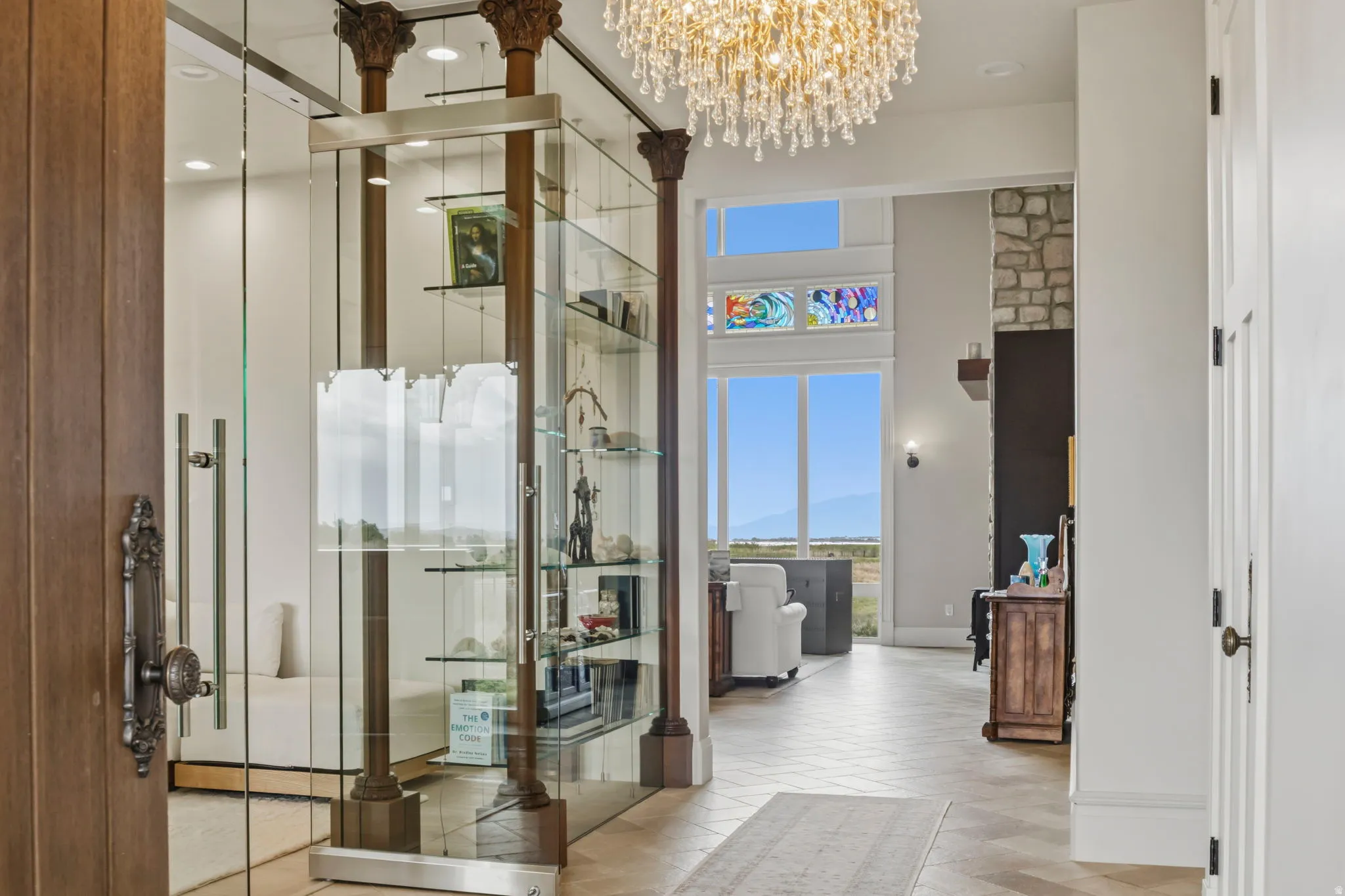 Grand entryway featuring a large crystal chandelier, tile flooring, and a glass-enclosed library