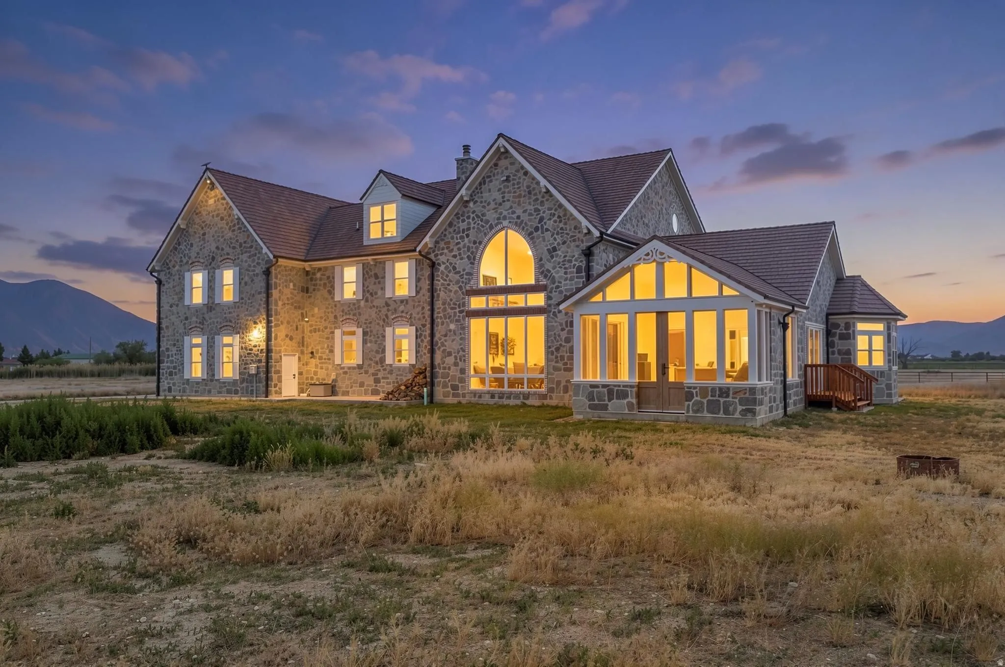 Rear of the Estate. Stone exterior with a prominent arched window and dormer windows. Outdoor kitchen attached.