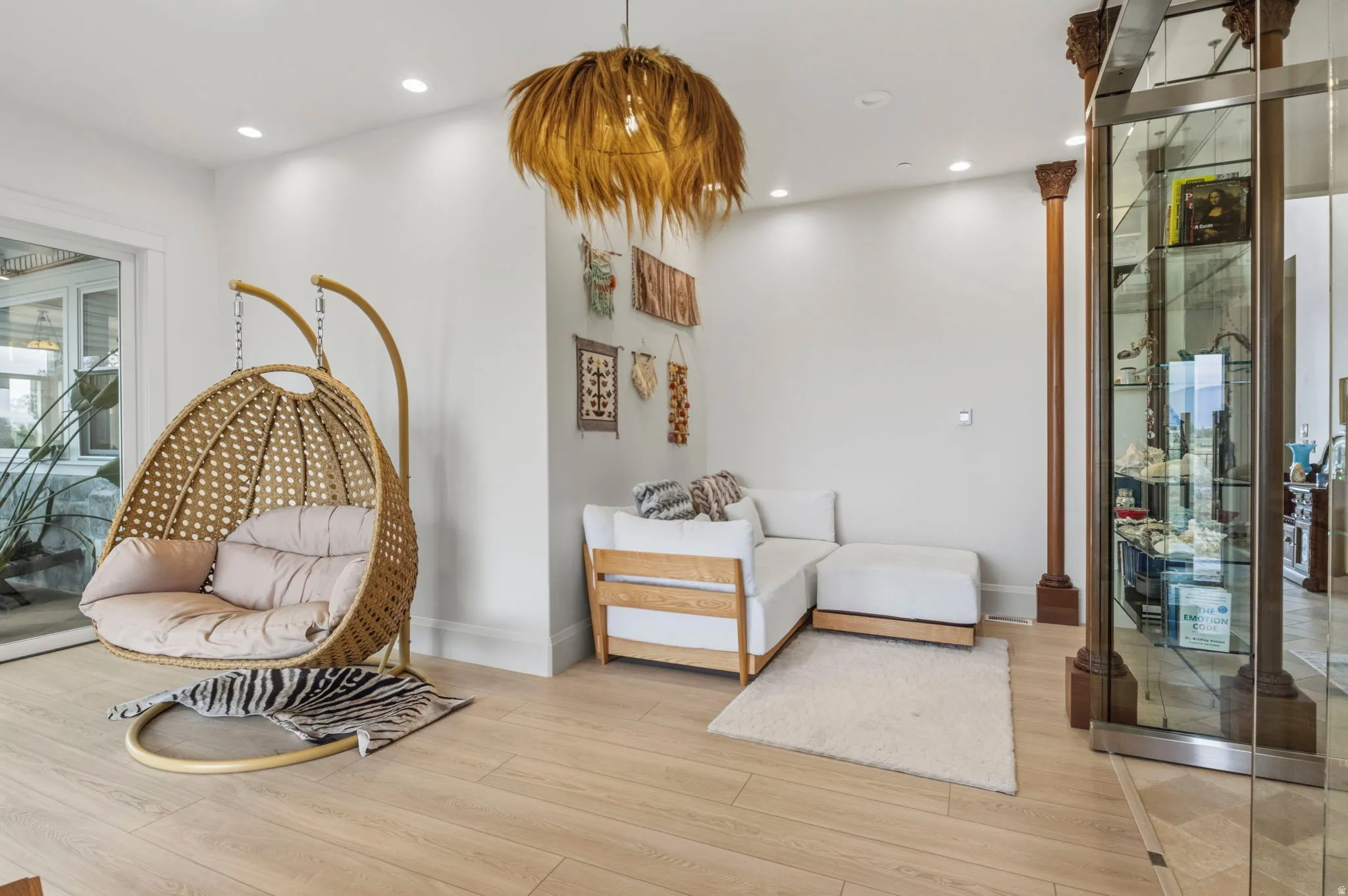 Light wood-finish flooring with recessed ceiling lighting, a decorative pendant light fixture, and a built-in display case with glass shelving. Peaceful Library with ample natural light.