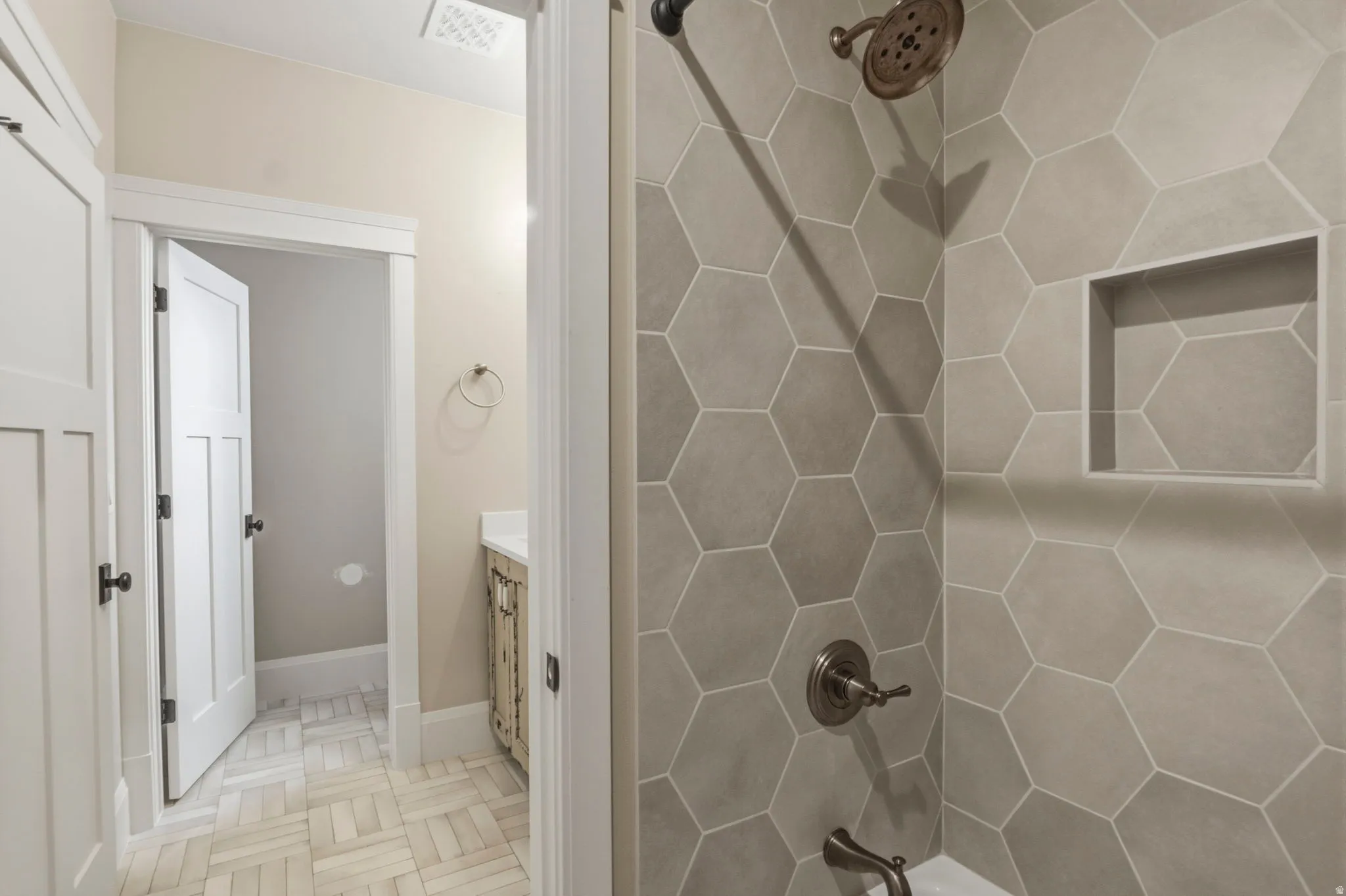 Shower featuring large hexagonal wall tiles, integrated shower niche, and bronze fixtures