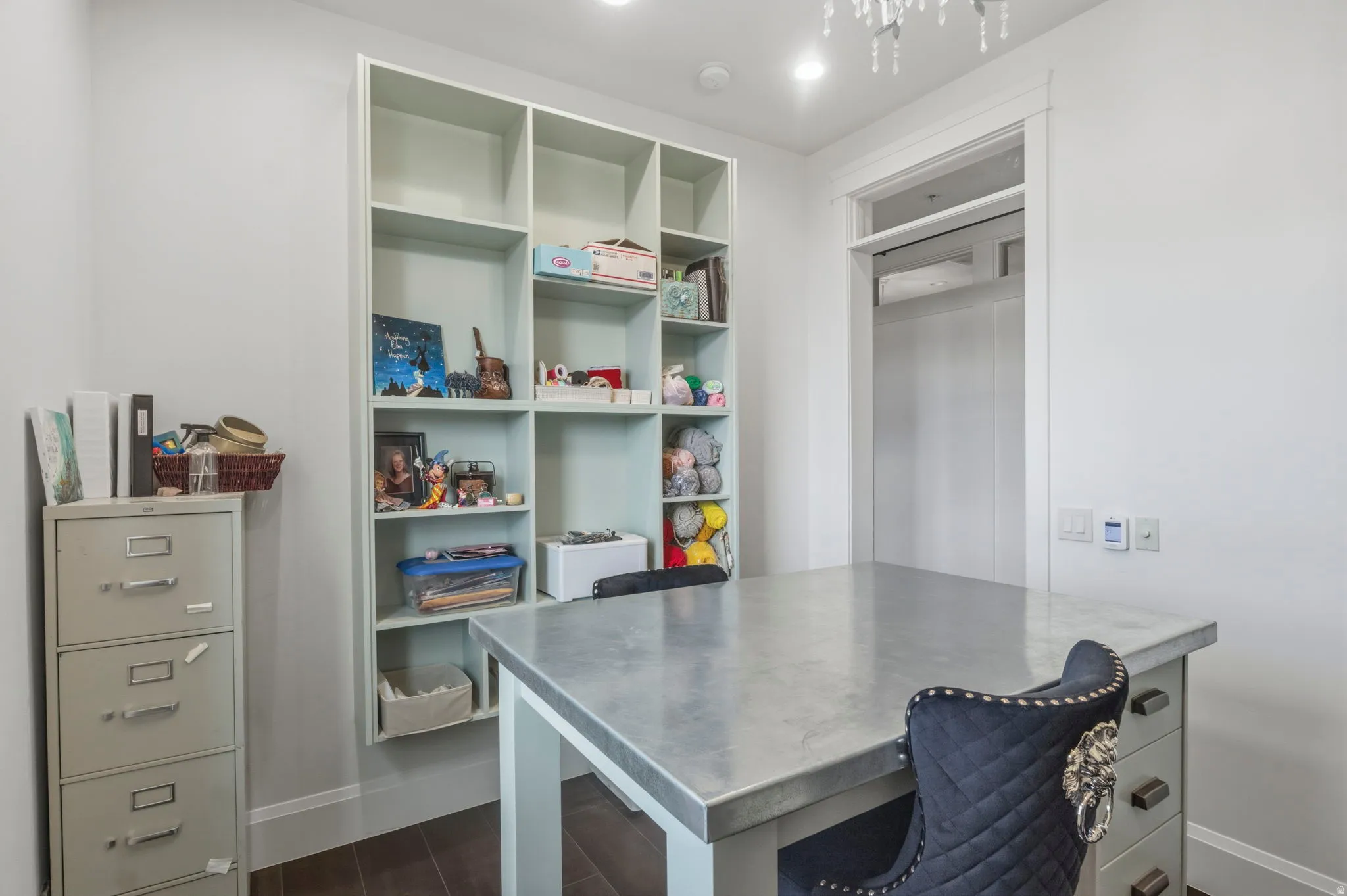 Integrated shelving unit with multiple compartments, a built-in countertop work surface, recessed lighting, and dark wood-finish flooring. This room doubles as an office and craft room.