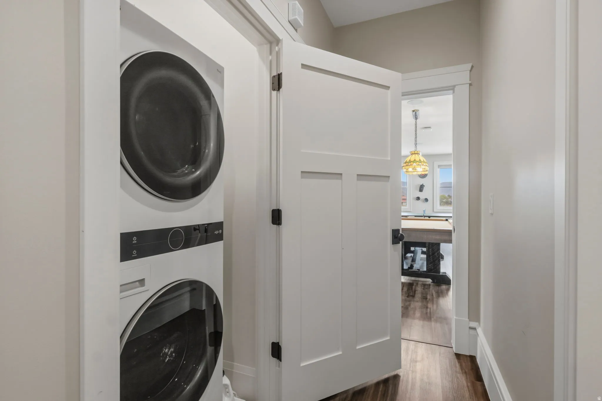 Stackable washer and dryer unit, white paneled interior door with dark hardware, light gray walls, and wood-finish flooring