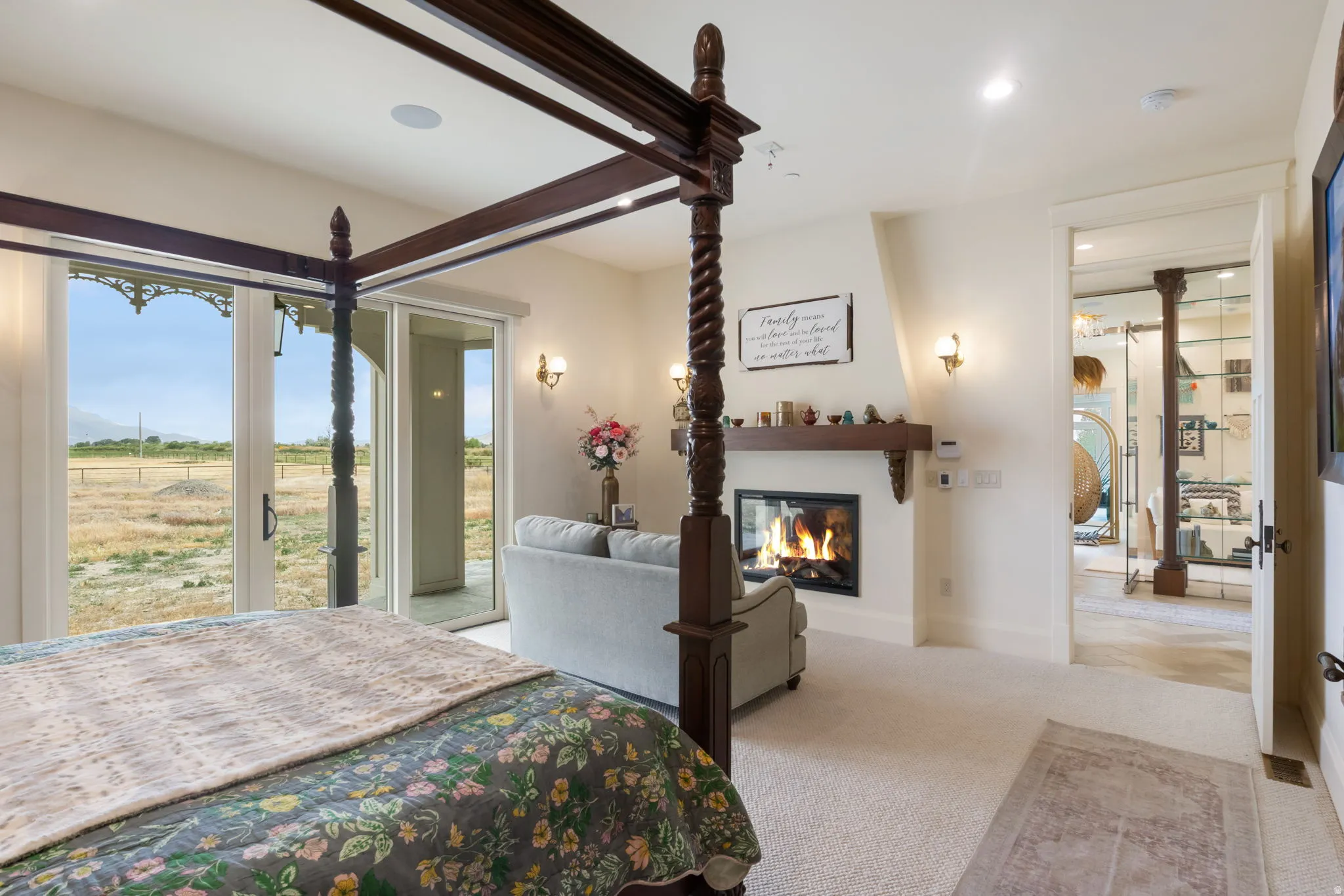 Spacious room featuring a fireplace with a wood mantle, direct outdoor access through sliding glass doors, carpeted flooring, and wall sconces