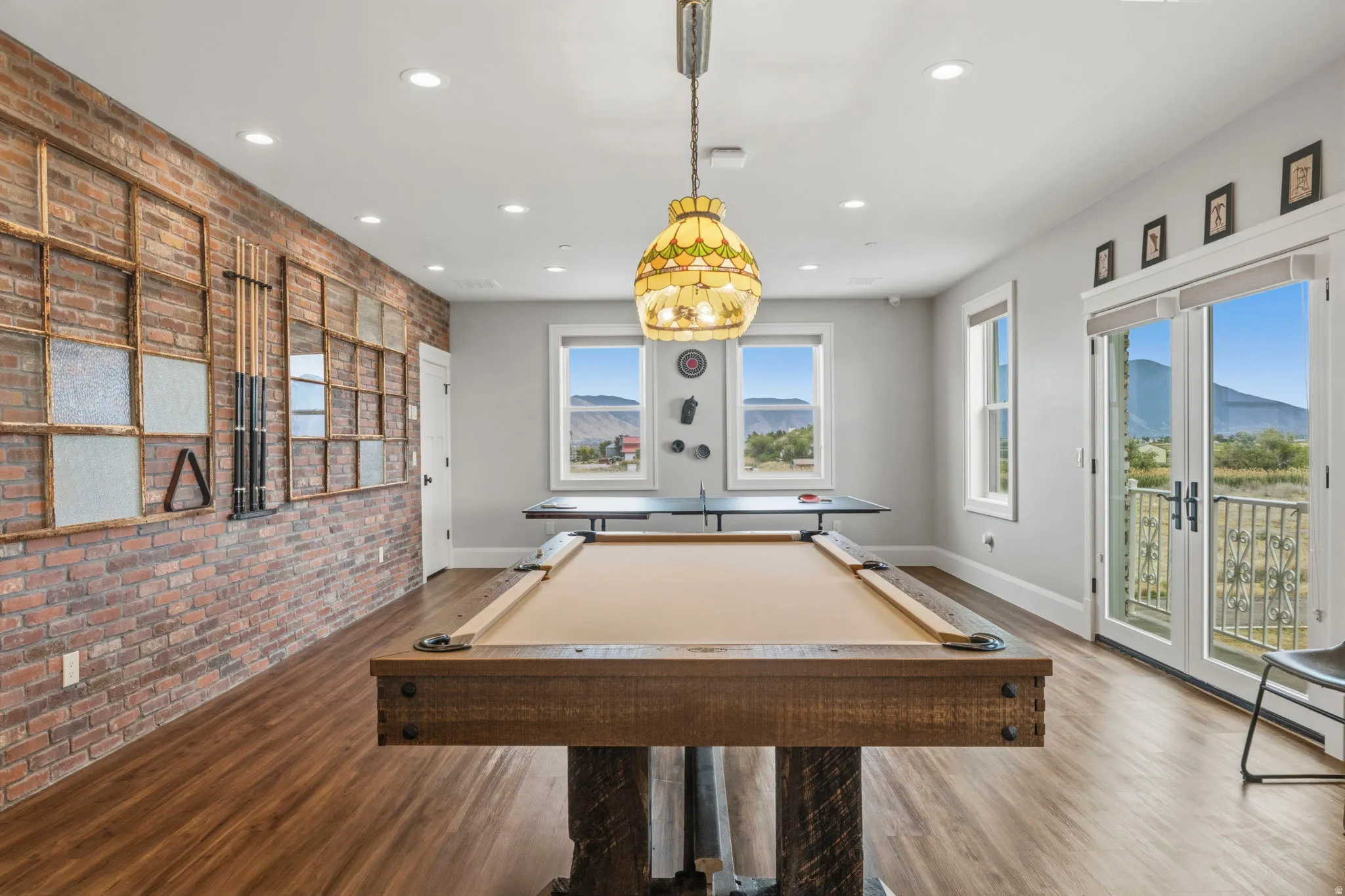 Spacious recreation room featuring wood-finish flooring, an exposed brick accent wall with framed glass inserts, and recessed lighting
