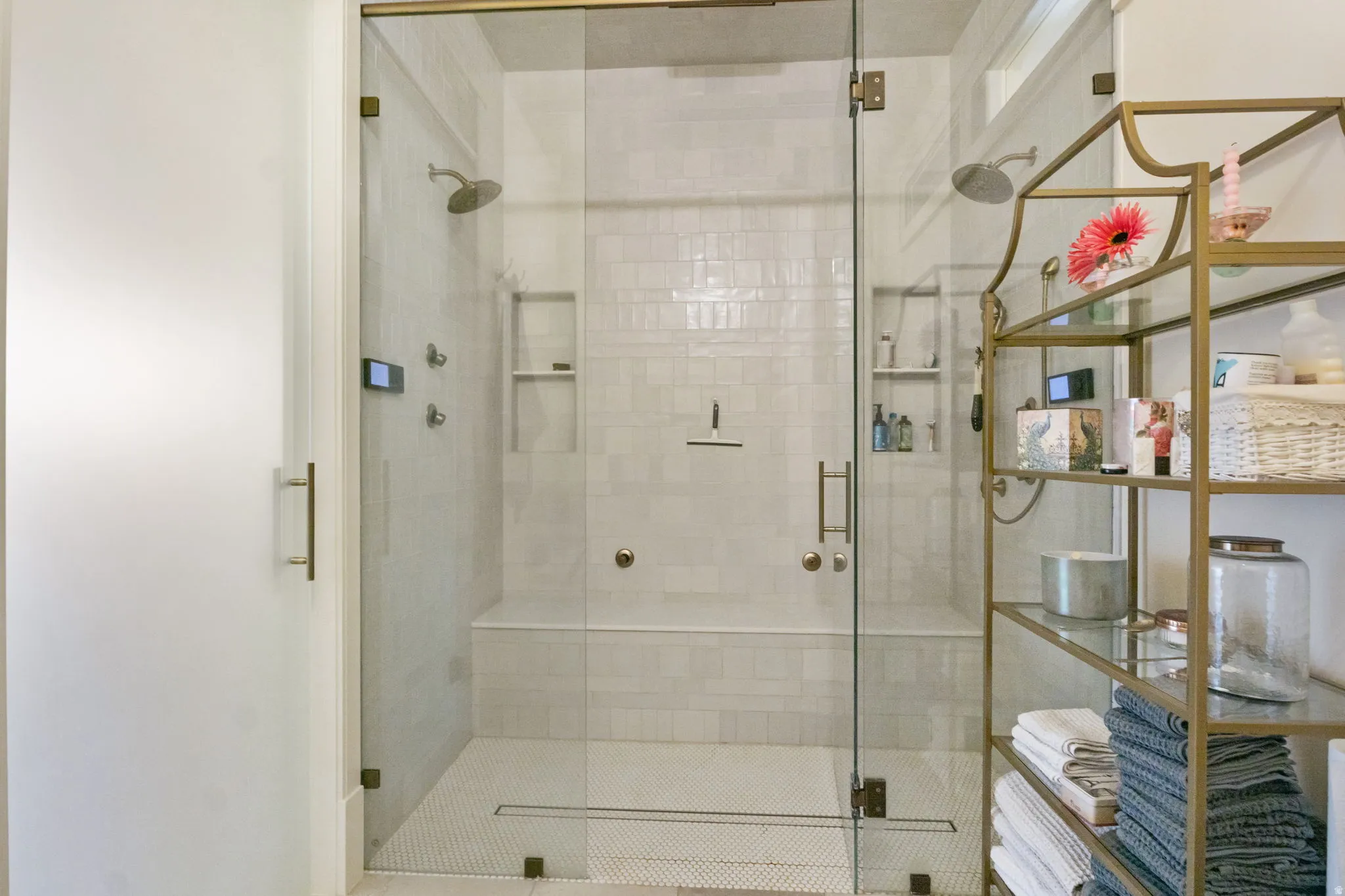Spacious glass-enclosed shower with multiple shower heads, integrated bench seating, and recessed shelving